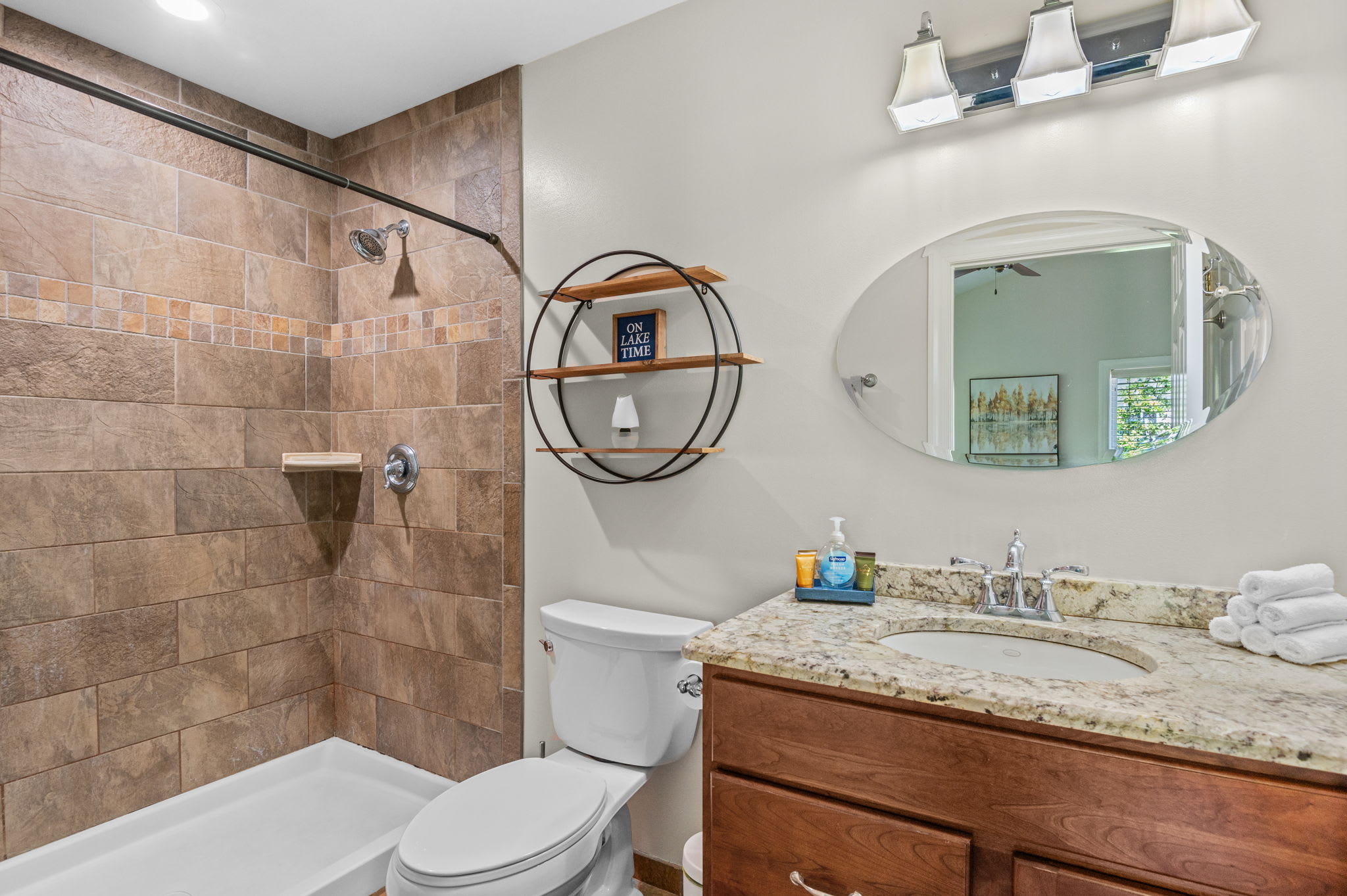 Full bathroom with a tiled shower, wooden vanity, and decorative round mirror