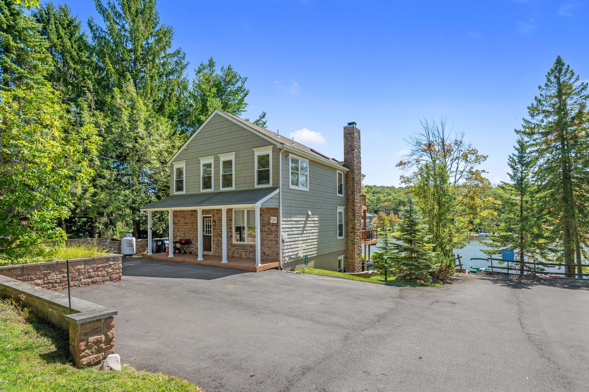 Front view of the lake house with a covered porch, stone walkway, and mature trees
