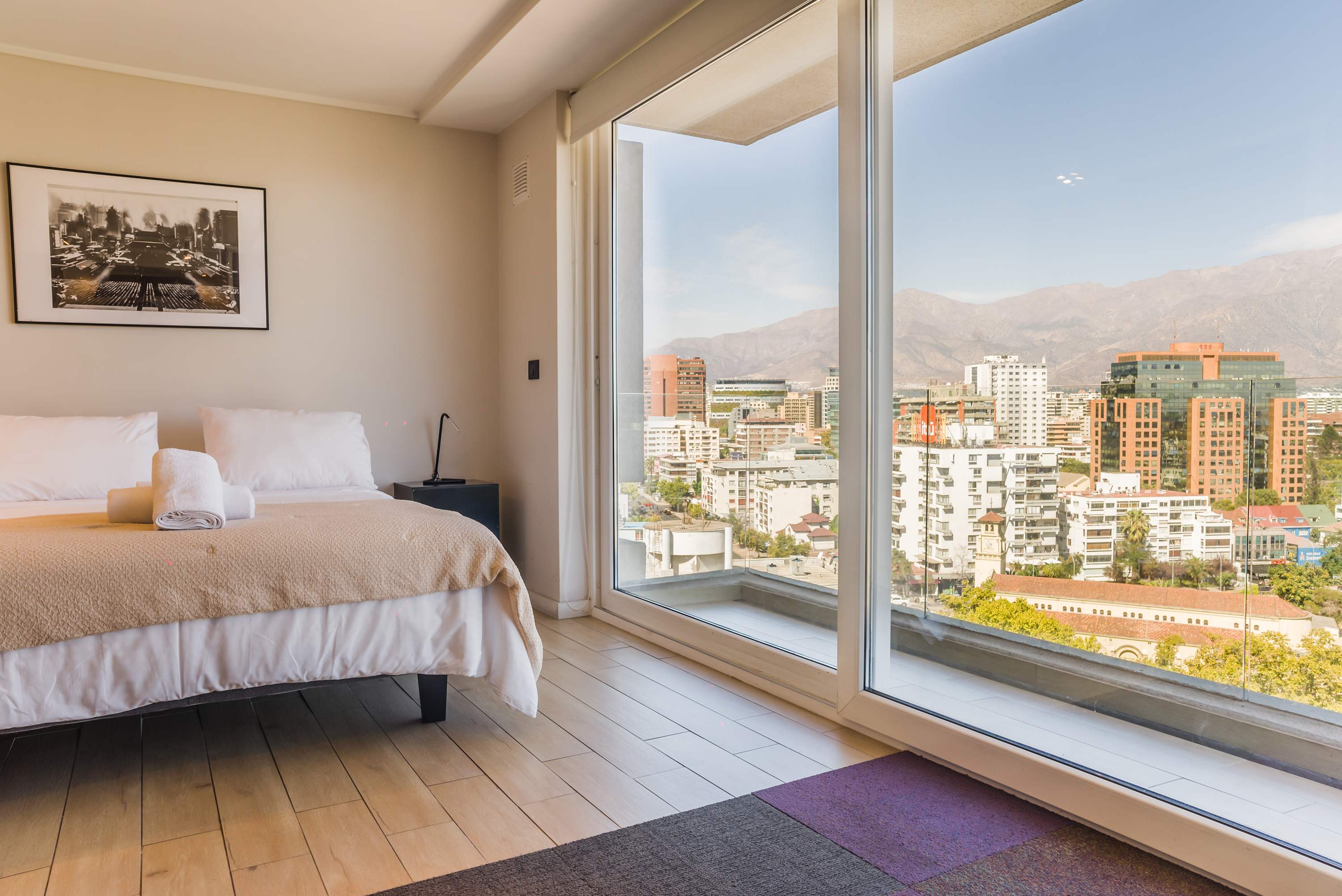 Relax in a cozy bedroom with breathtaking city and mountain views from a large window.