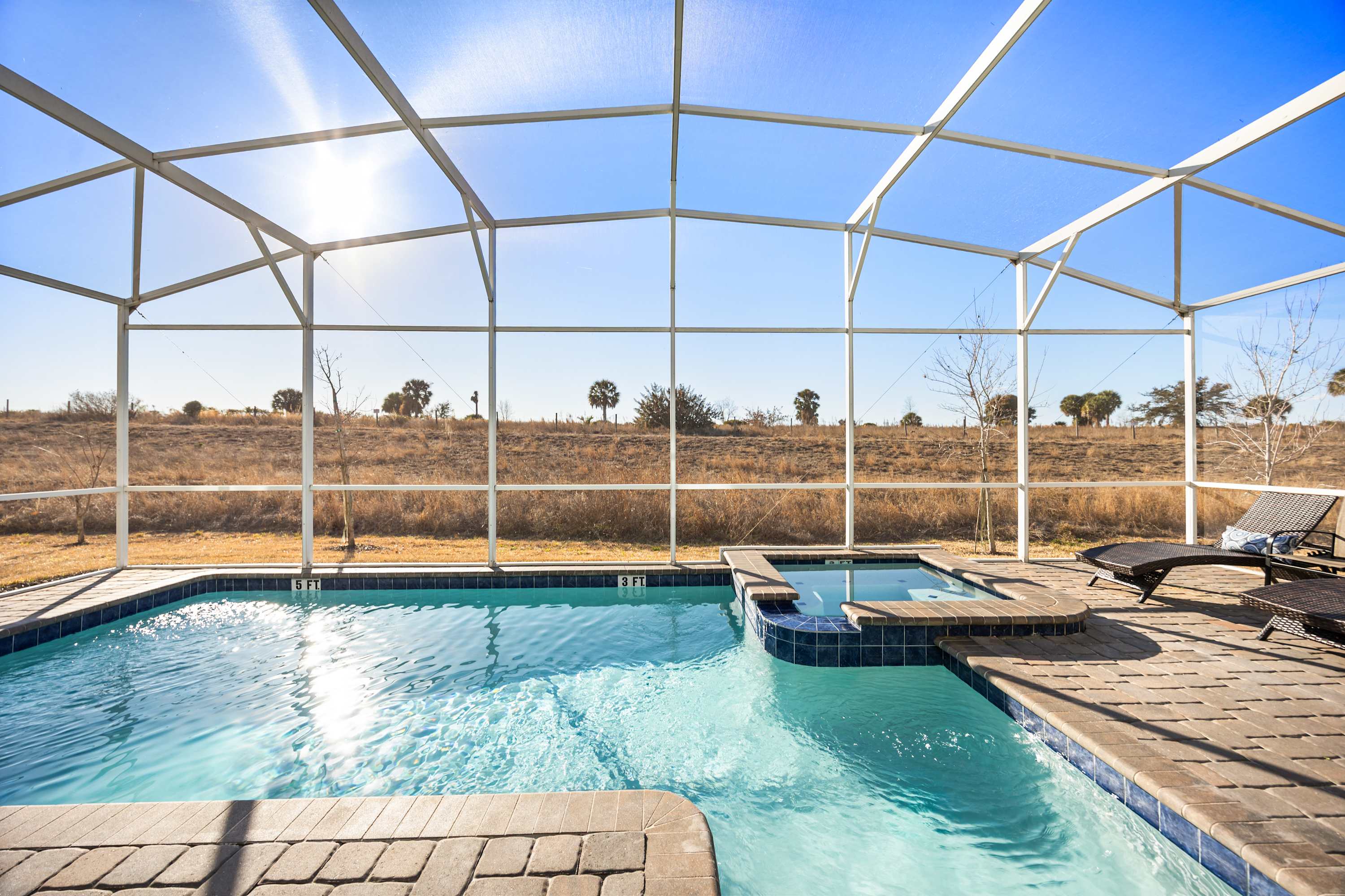 Relax in your private screened-in pool and hot tub with stunning open landscape views, perfect for unwinding under the sun.
