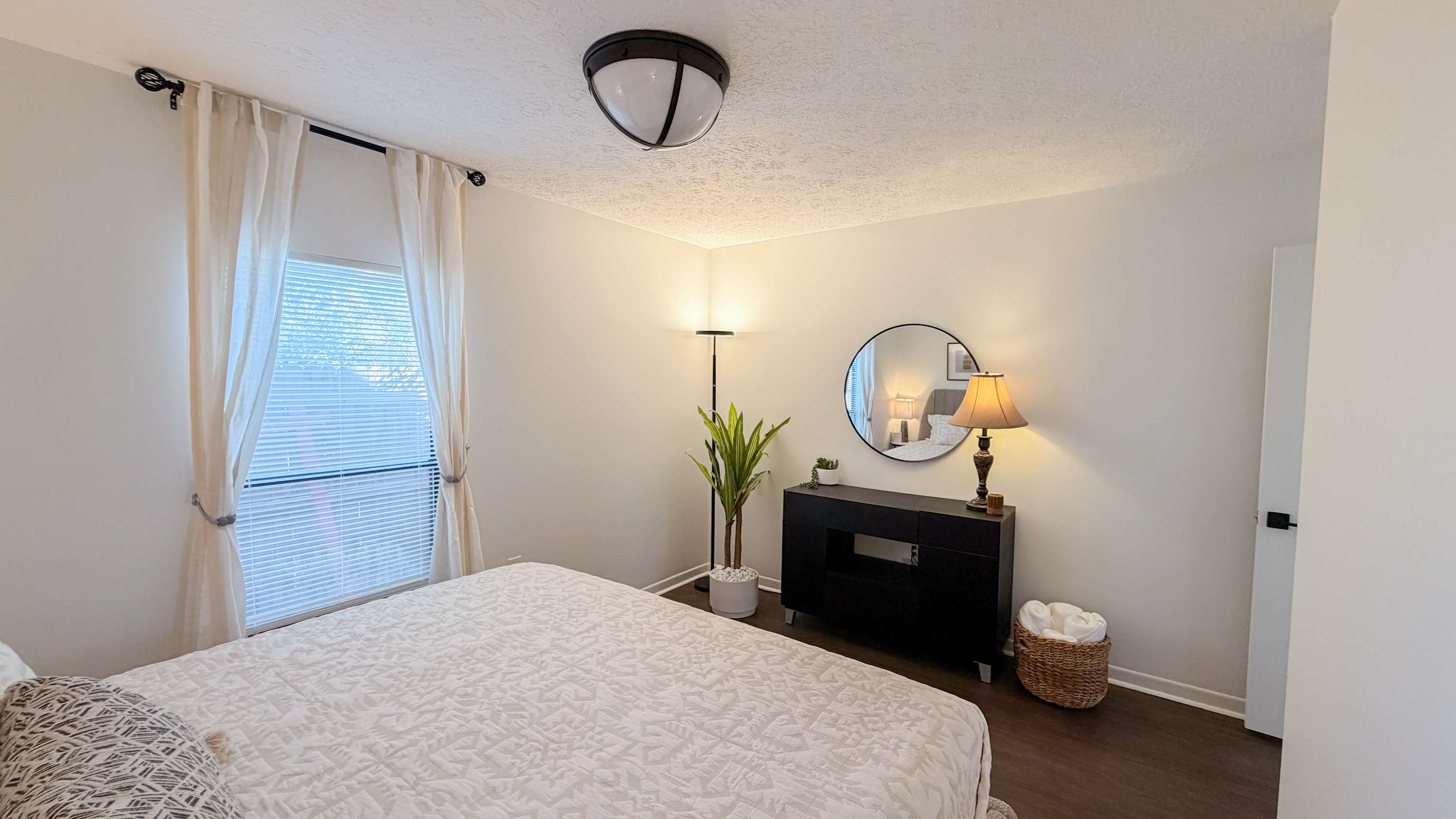300 W 23rd Pl – Bright bedroom with a bed, dresser, plant, lamp, and window with sheer curtains.