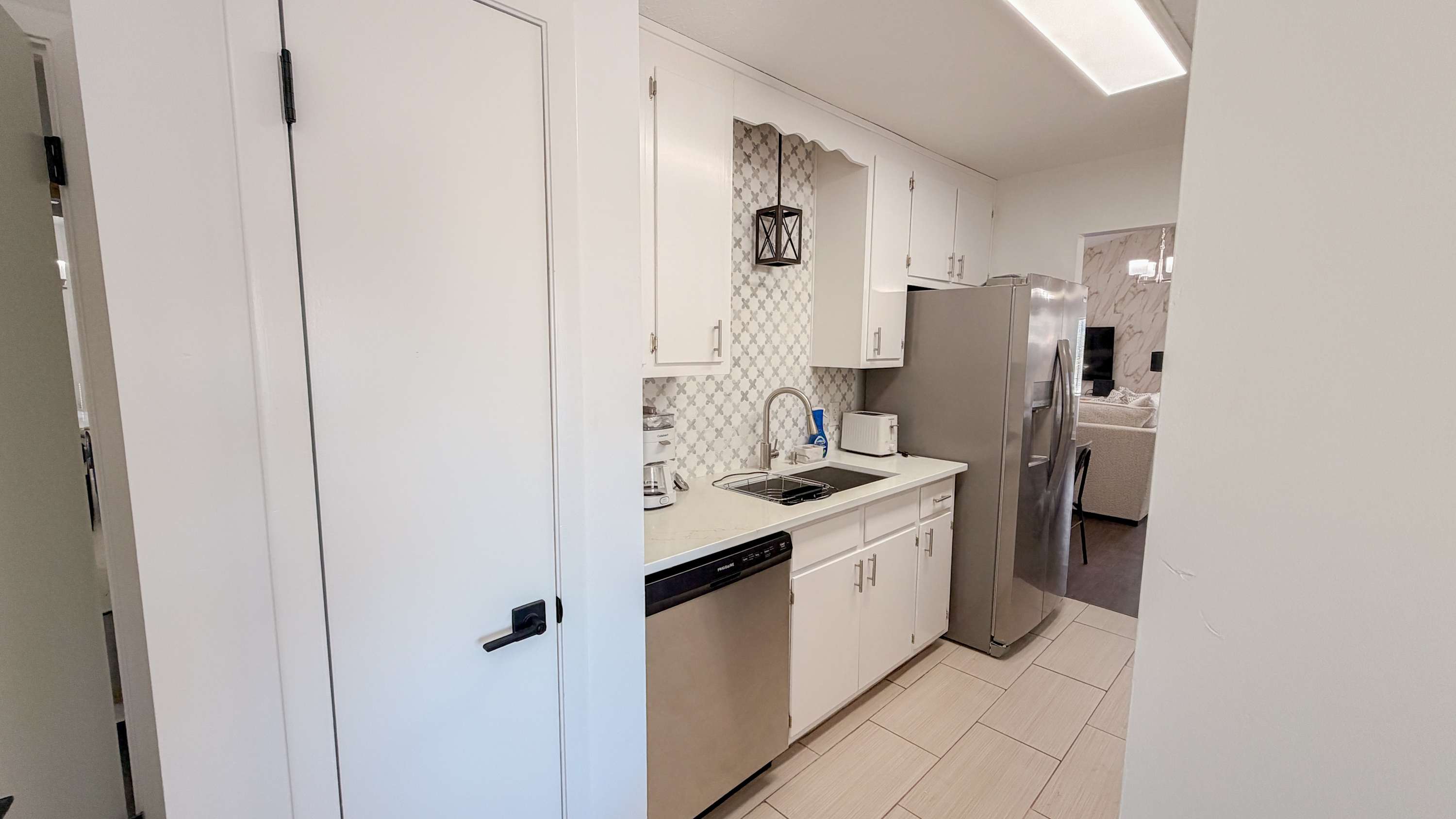 300 W 23rd Pl – Compact kitchen with white cabinets, stainless steel appliances, and tile flooring, leading to a living area.