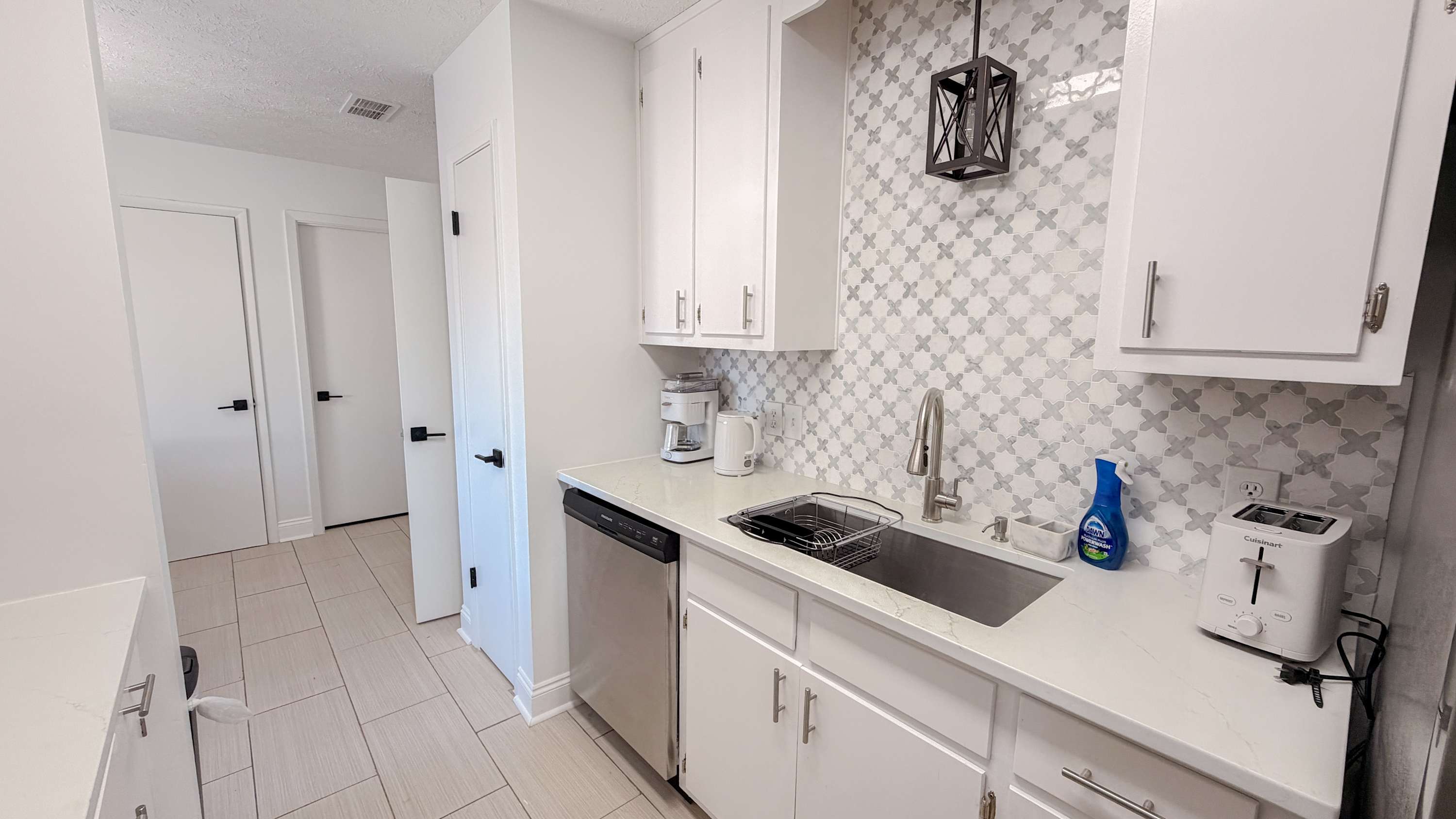 300 W 23rd Pl – Kitchen with white cabinets, stainless steel appliances, and tiled backsplash. Two doors visible in background.