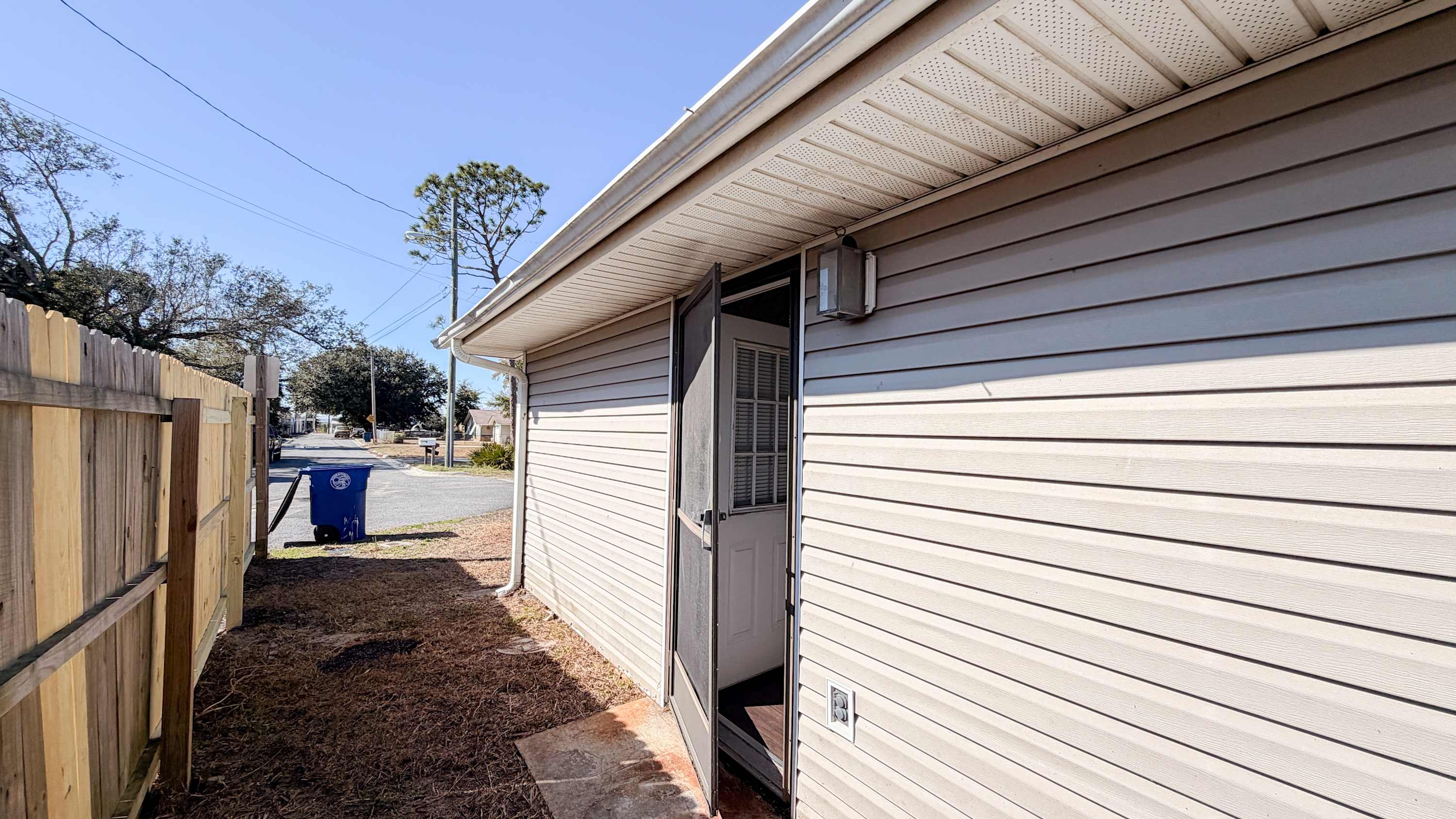 300 W 23rd Pl – Side view of vacation rental exterior with open screen door and pathway, street visible in the background.