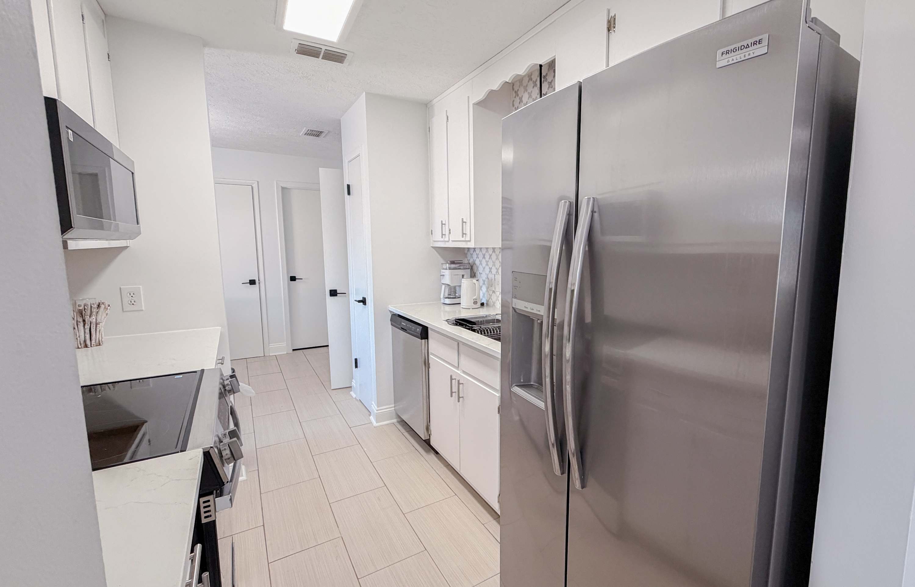 300 W 23rd Pl – Modern kitchen with stainless steel appliances, white cabinets, and light tile flooring.