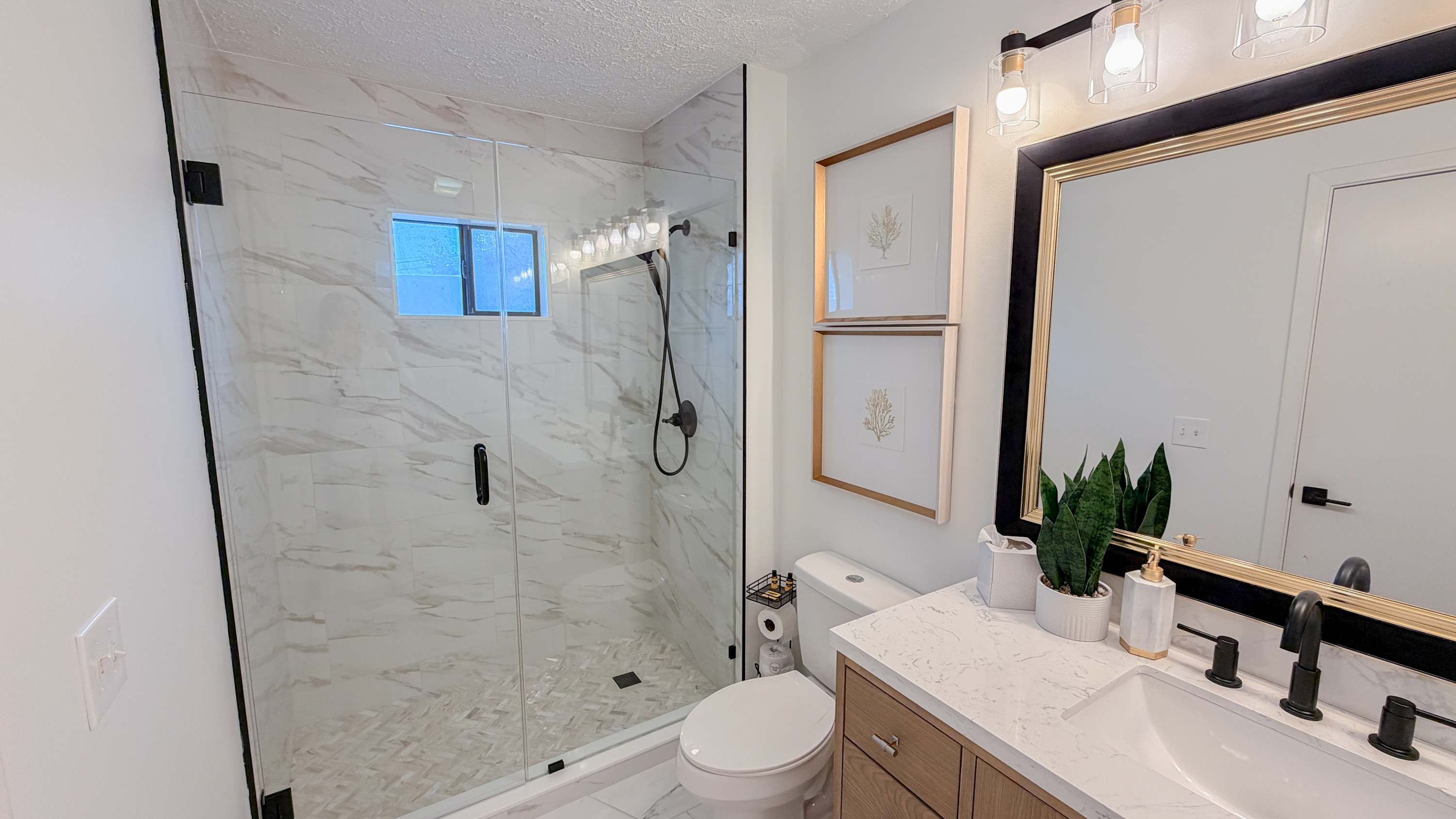 300 W 23rd Pl – Modern bathroom with glass shower, marble tiles, vanity sink, and framed artwork.