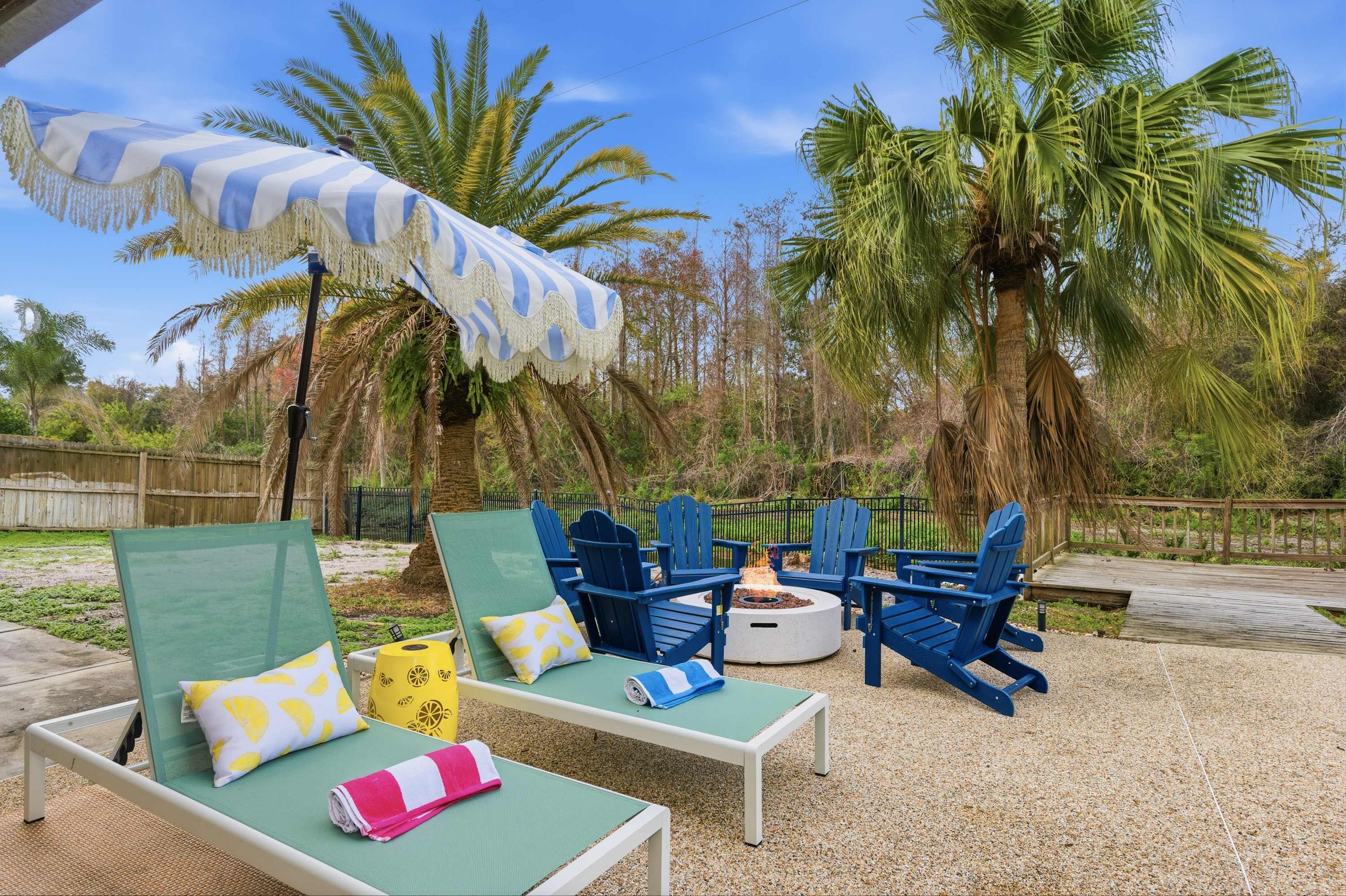 Lush backyard lounge w/ blue Adirondack chairs & swaying palms.