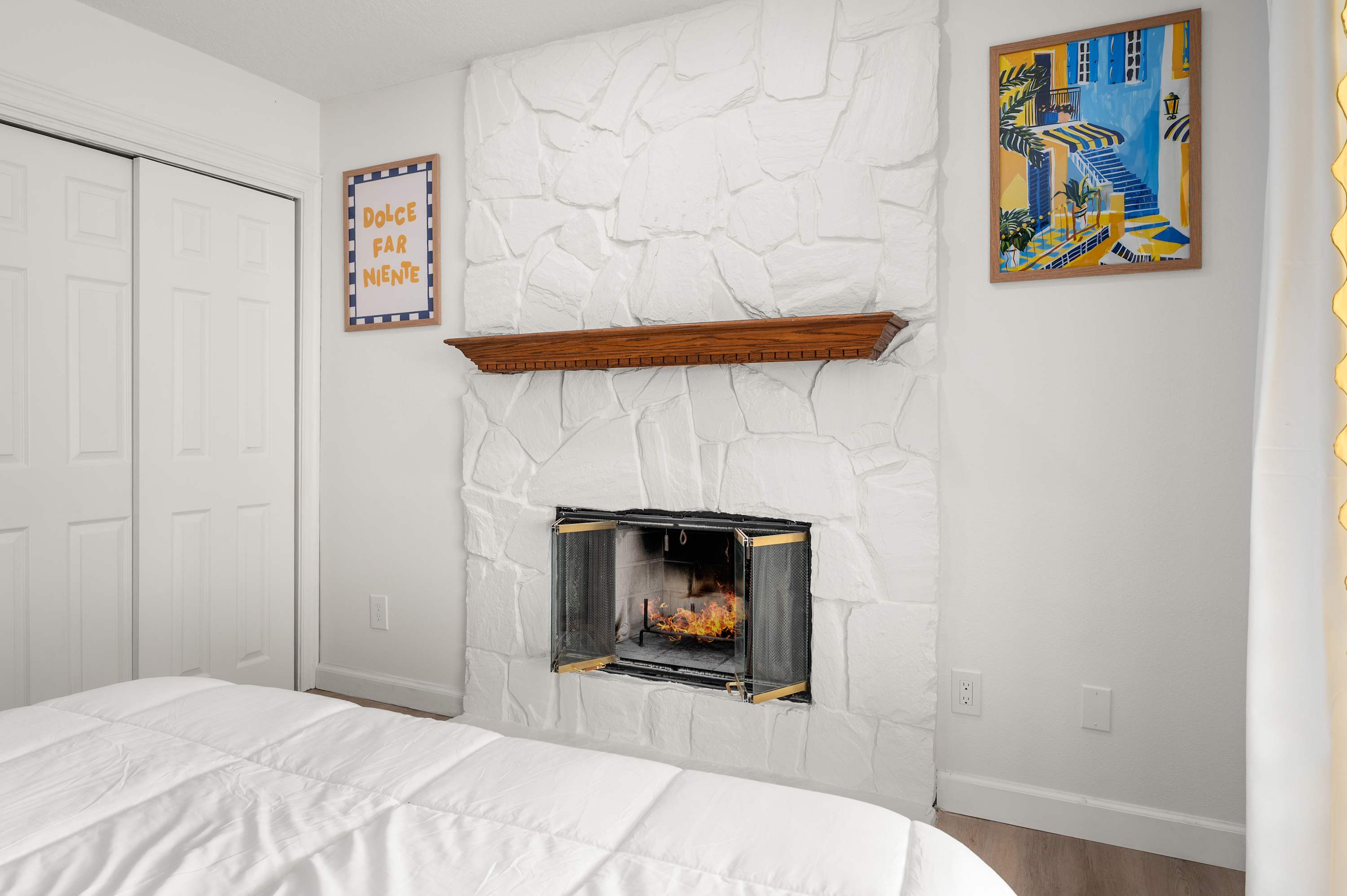 Bright bedroom w/ a bed, fireplace & warm natural light.