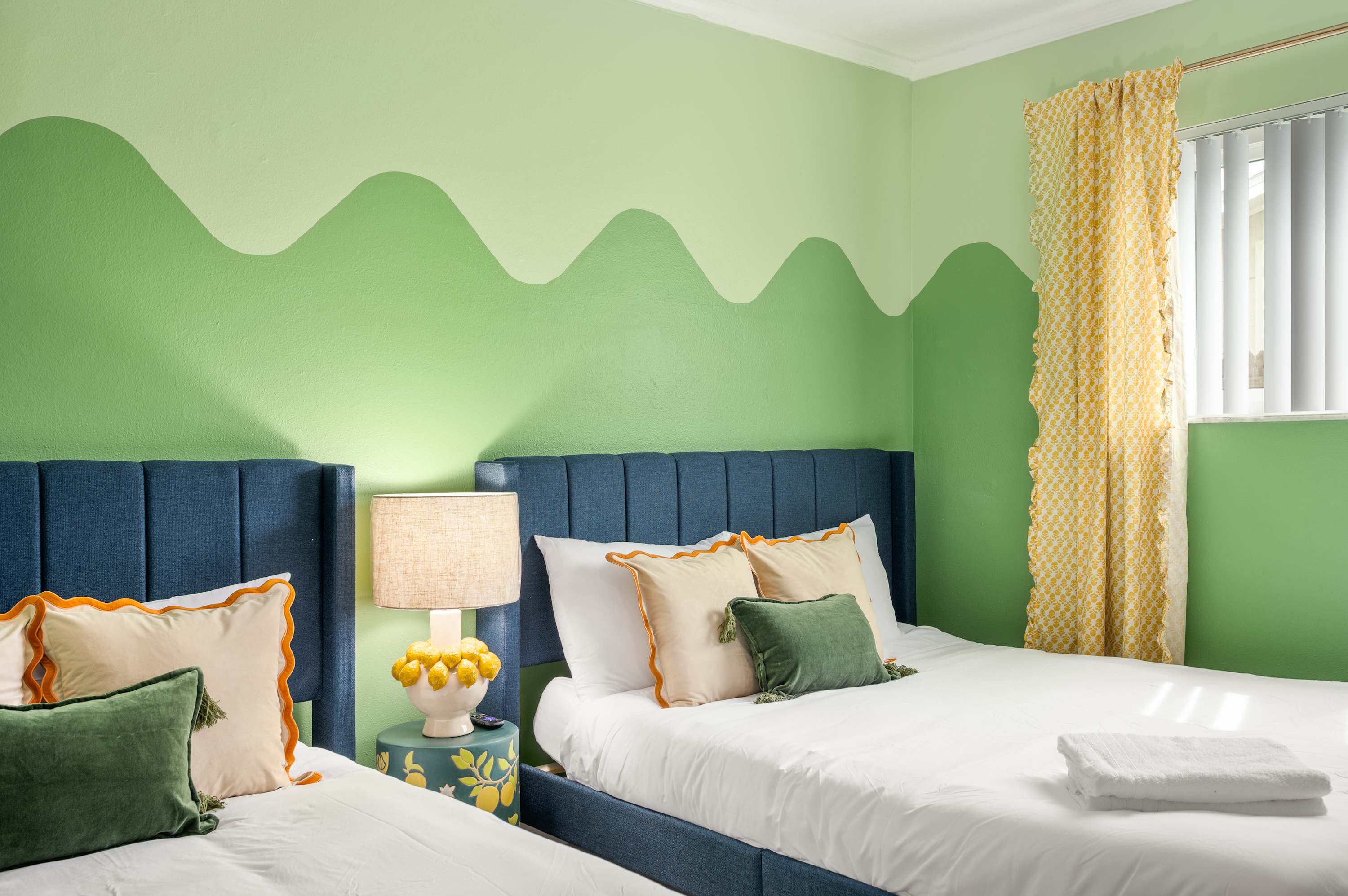 Whimsical bedroom w/ a painted mountain wall & two beds side by side.