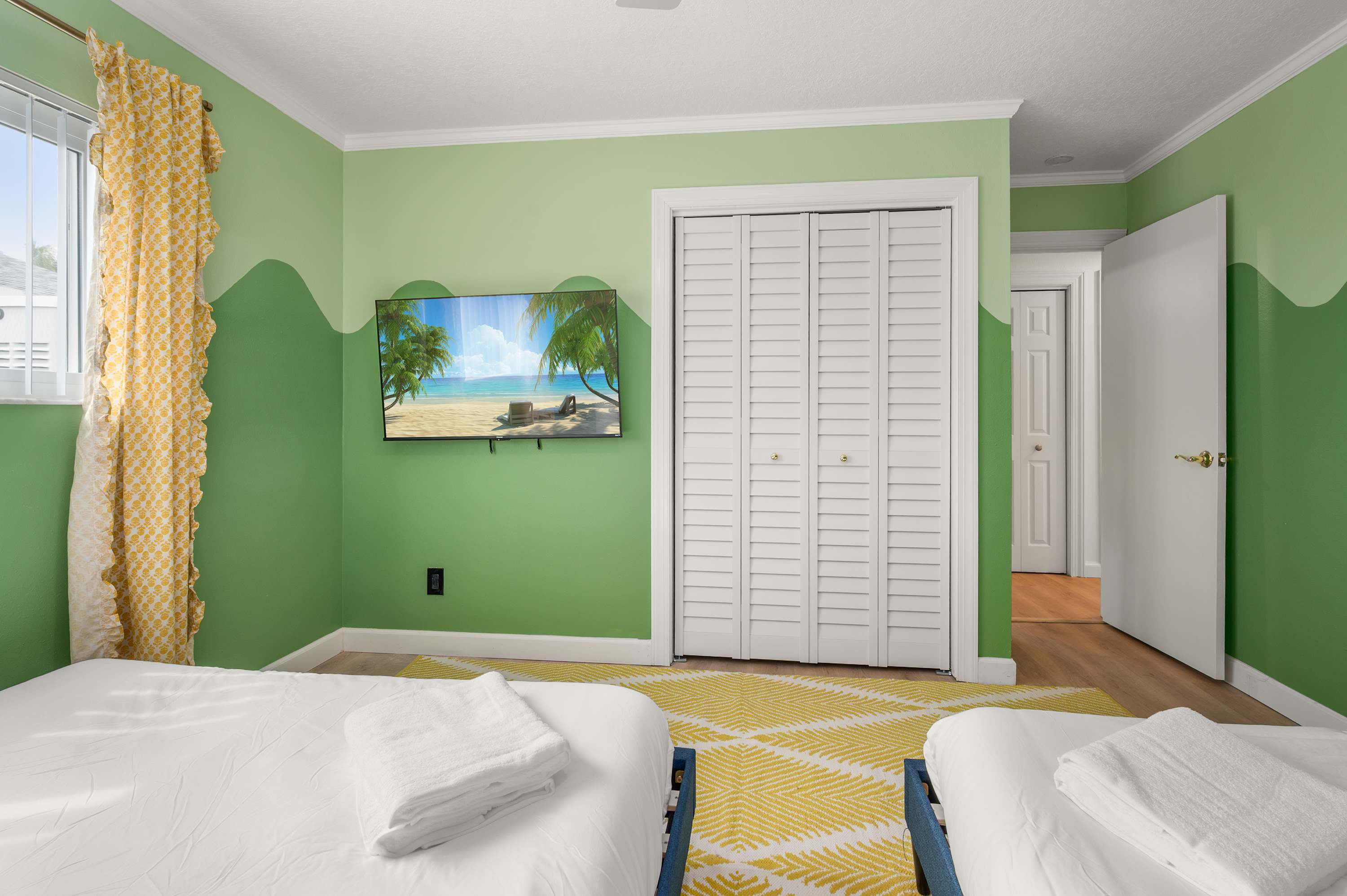 Bright bedroom w/ two beds, green accent wall & plenty of natural light.