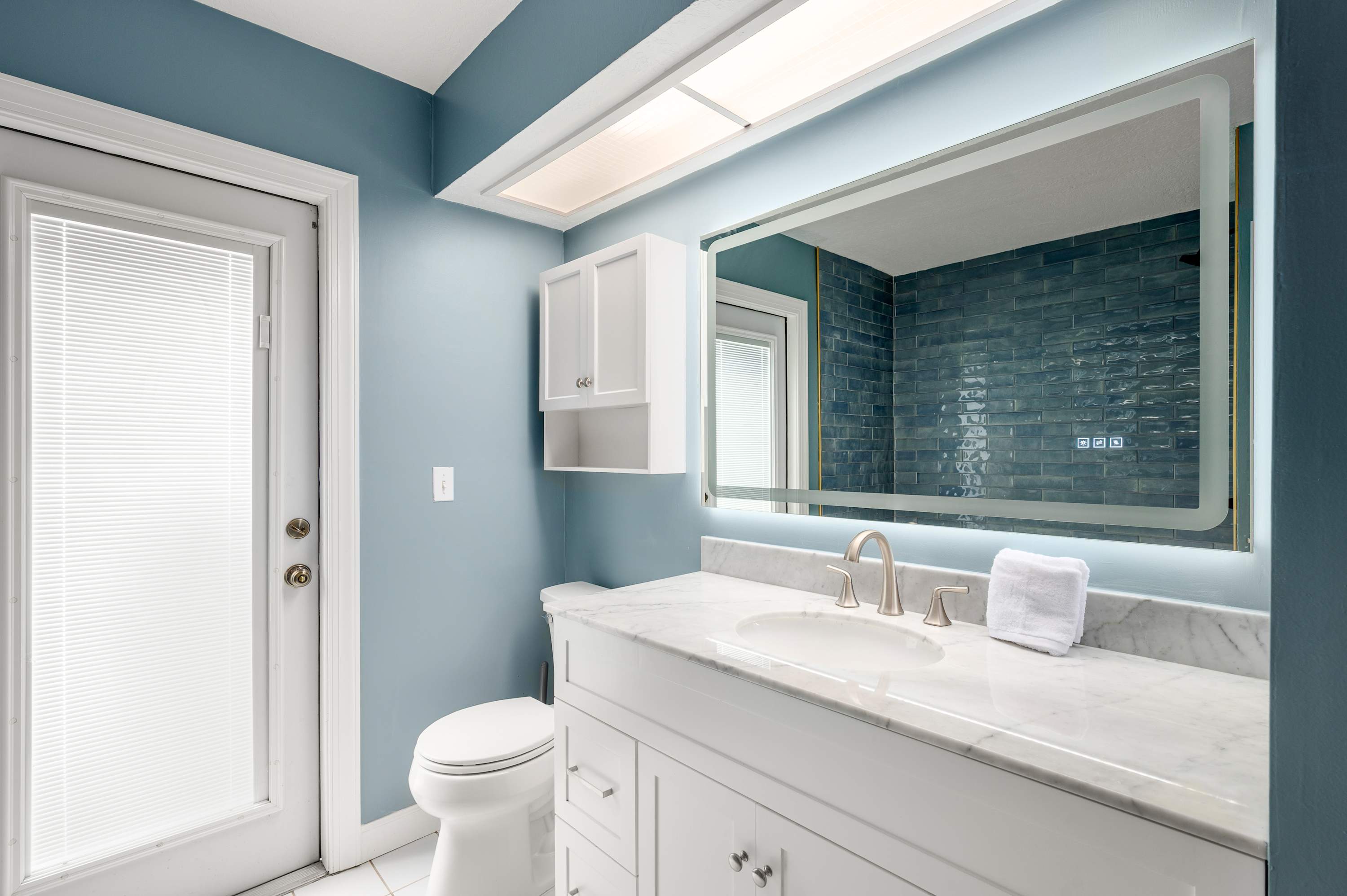Clean bathroom w/ tub, toilet & teal tile backsplash above the vanity.