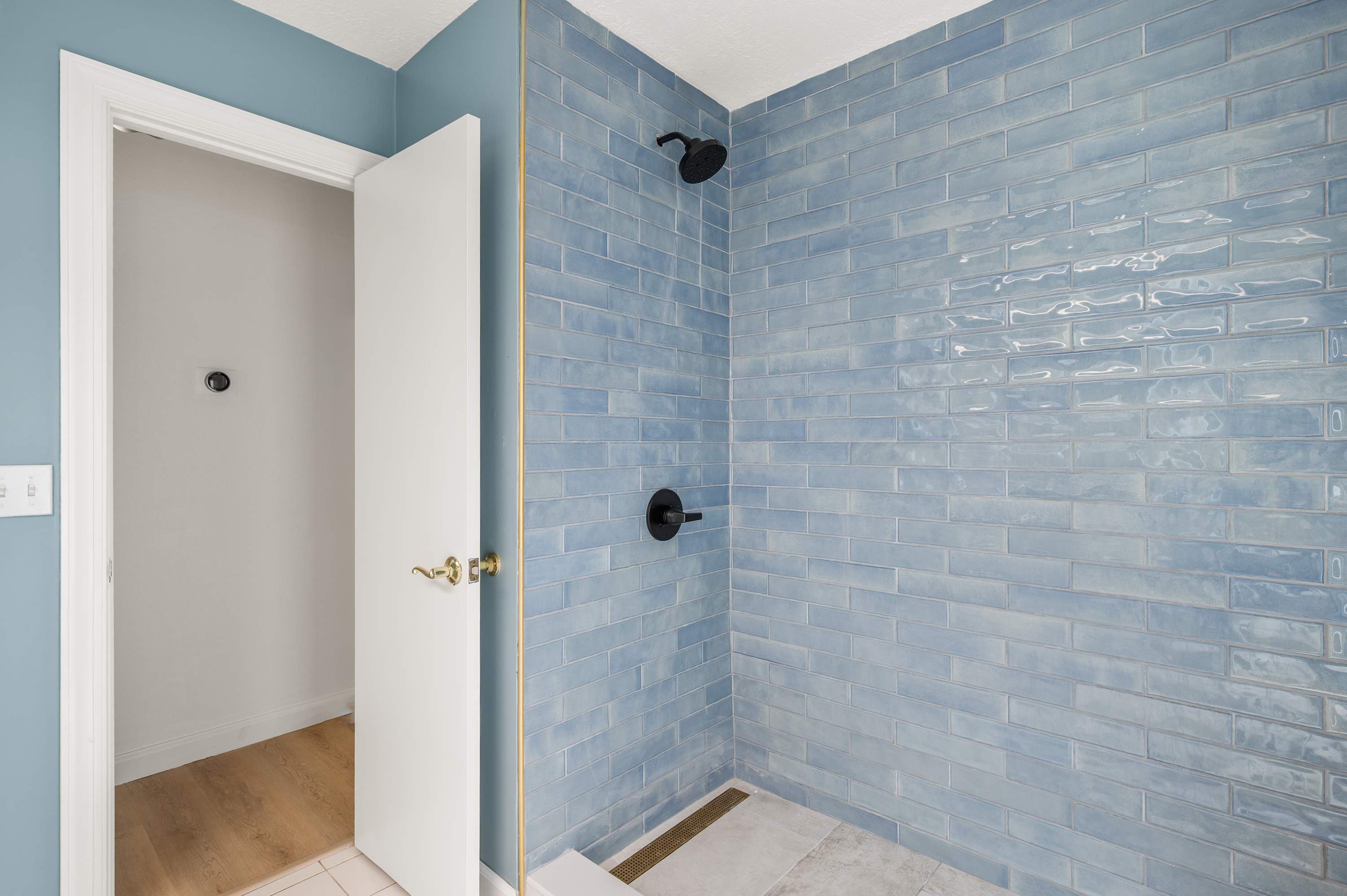 Walk-in shower w/ floor-to-ceiling blue tile & matte black fixtures.