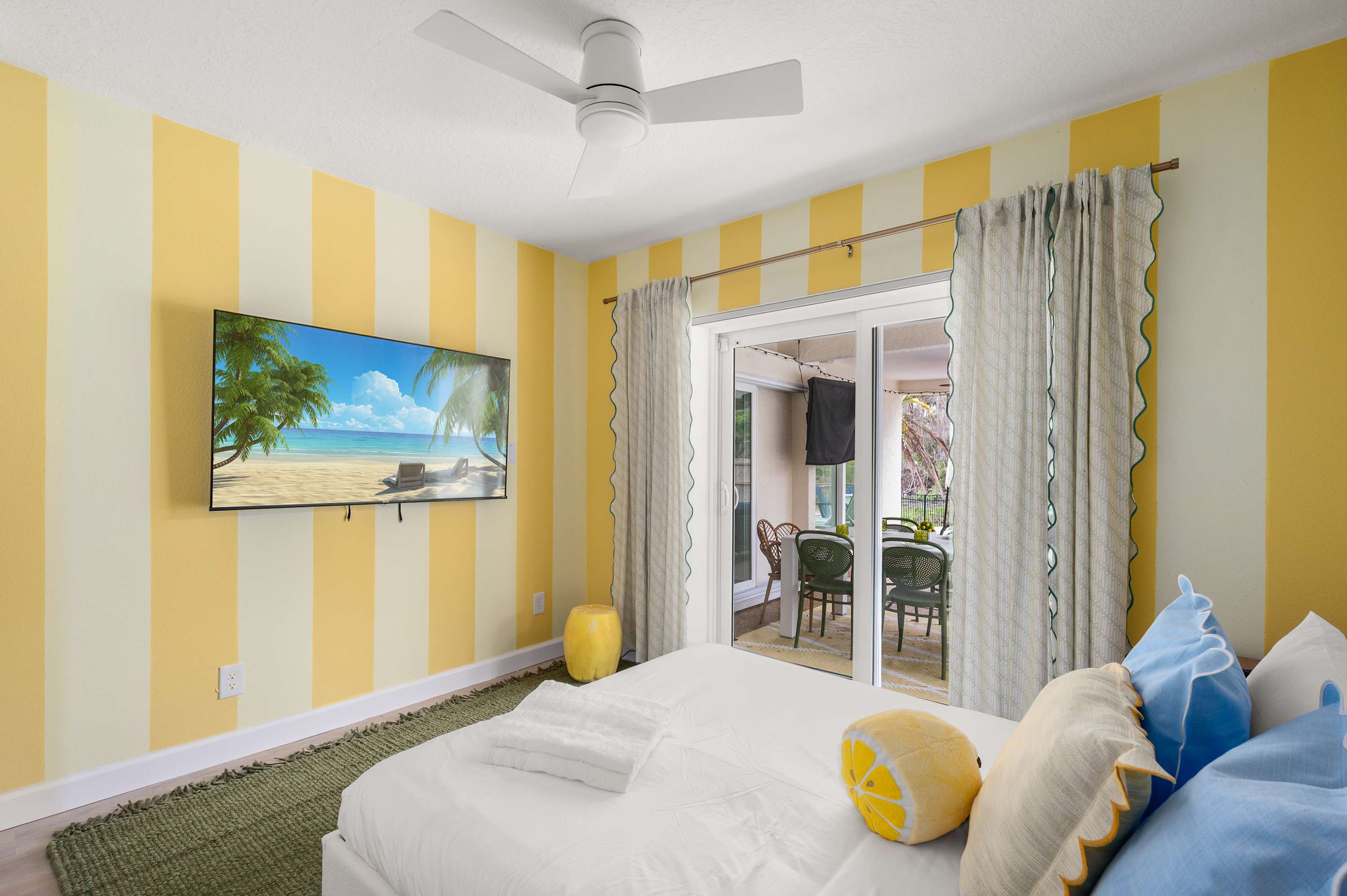 Cheerful bedroom w/ yellow striped walls, a bed & garden views.