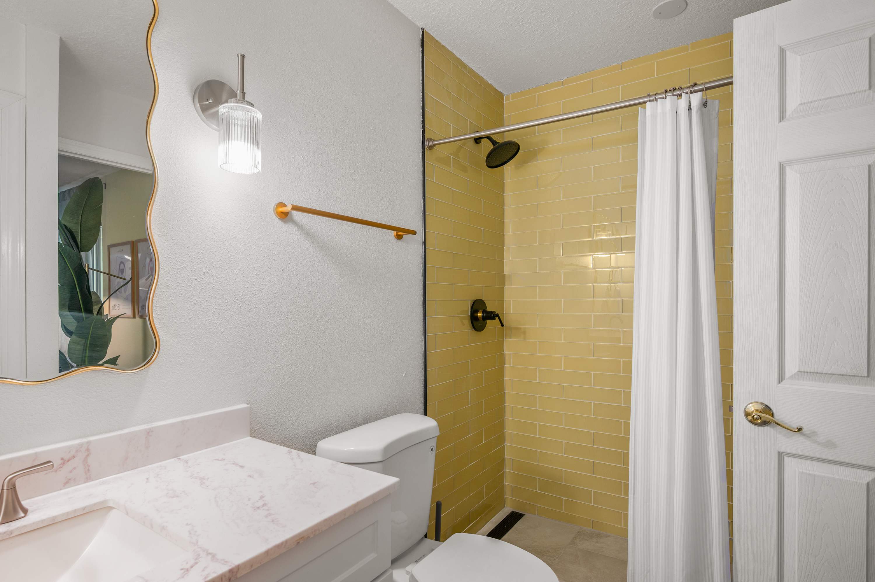 Bright bedroom w/ curtained shower, a bed & warm neutral tones.