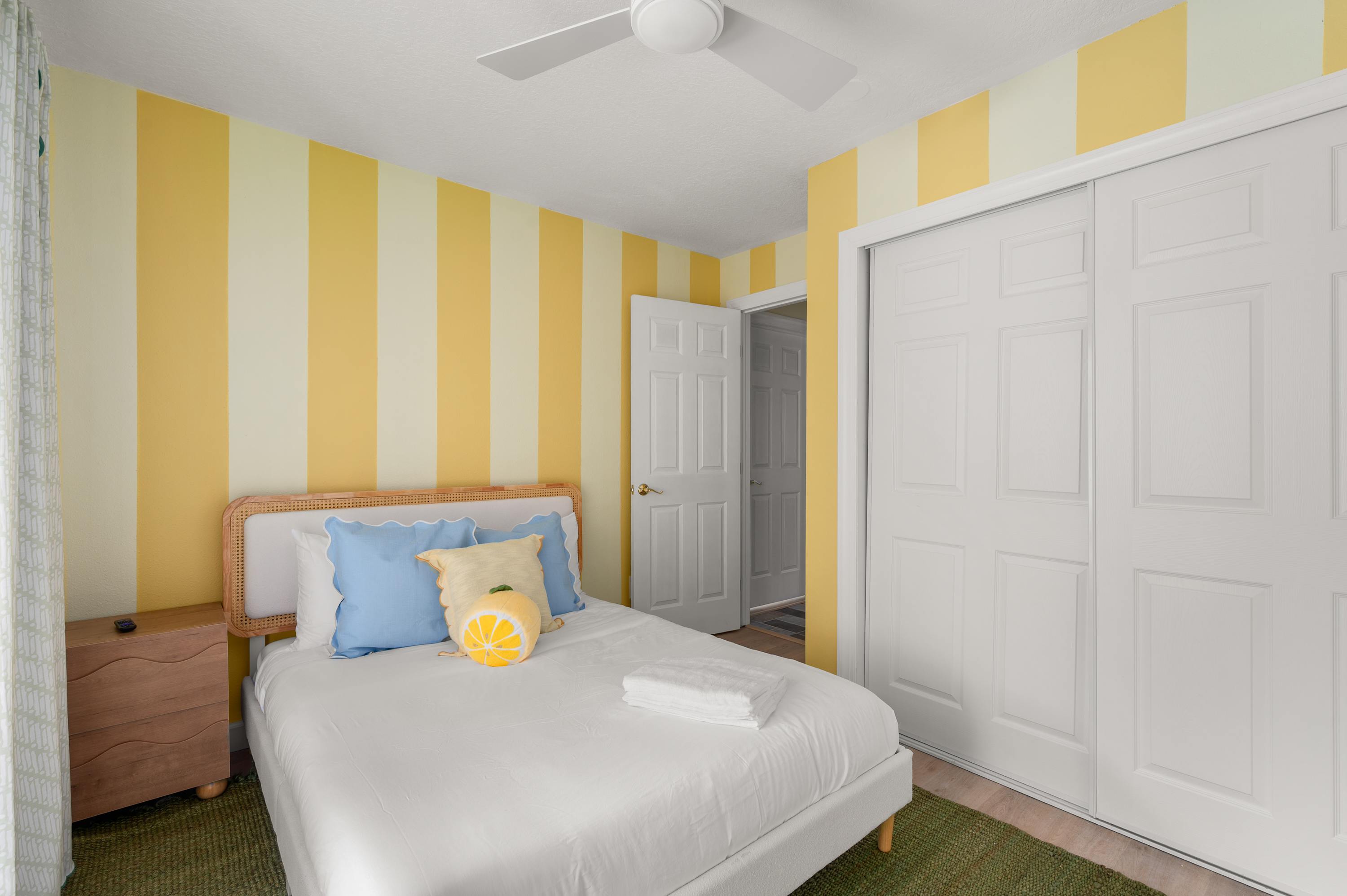 Yellow striped bedroom w/ a bed, closet & soft natural light.