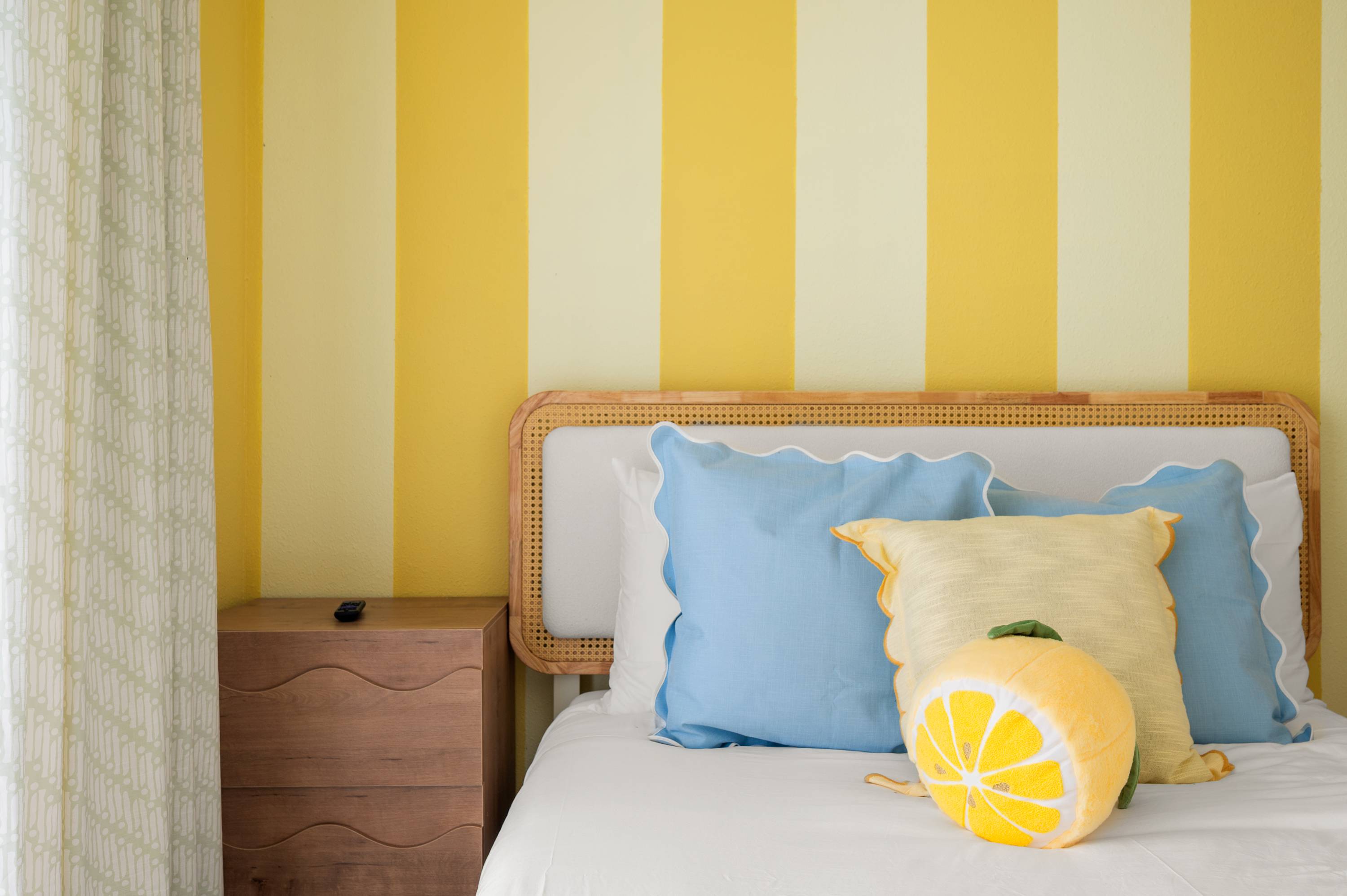 Sunny bedroom w/ yellow striped walls, blue accents & a cozy bed.