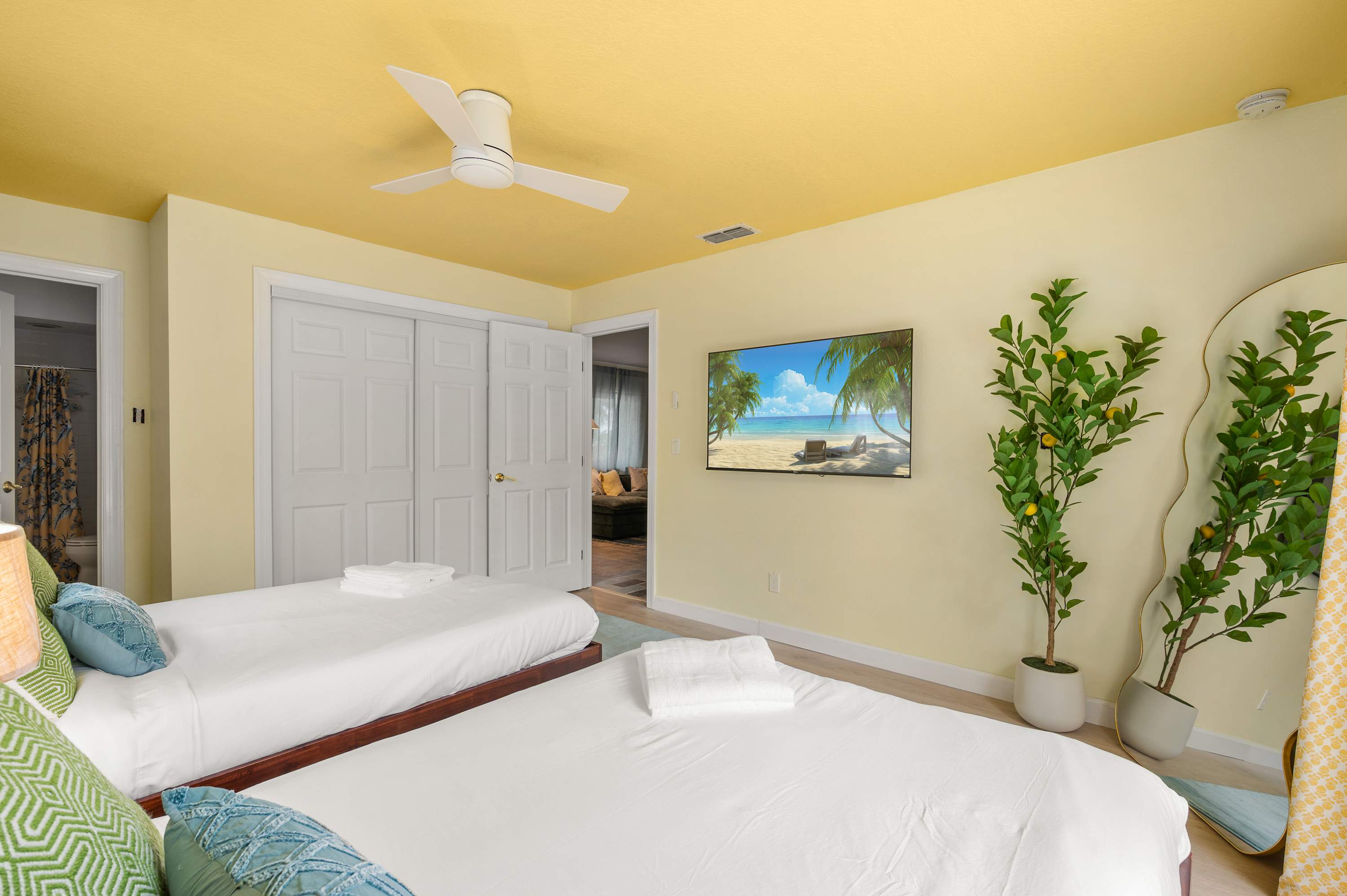 Airy bedroom w/ ceiling fan, a centered bed & lush greenery outside.