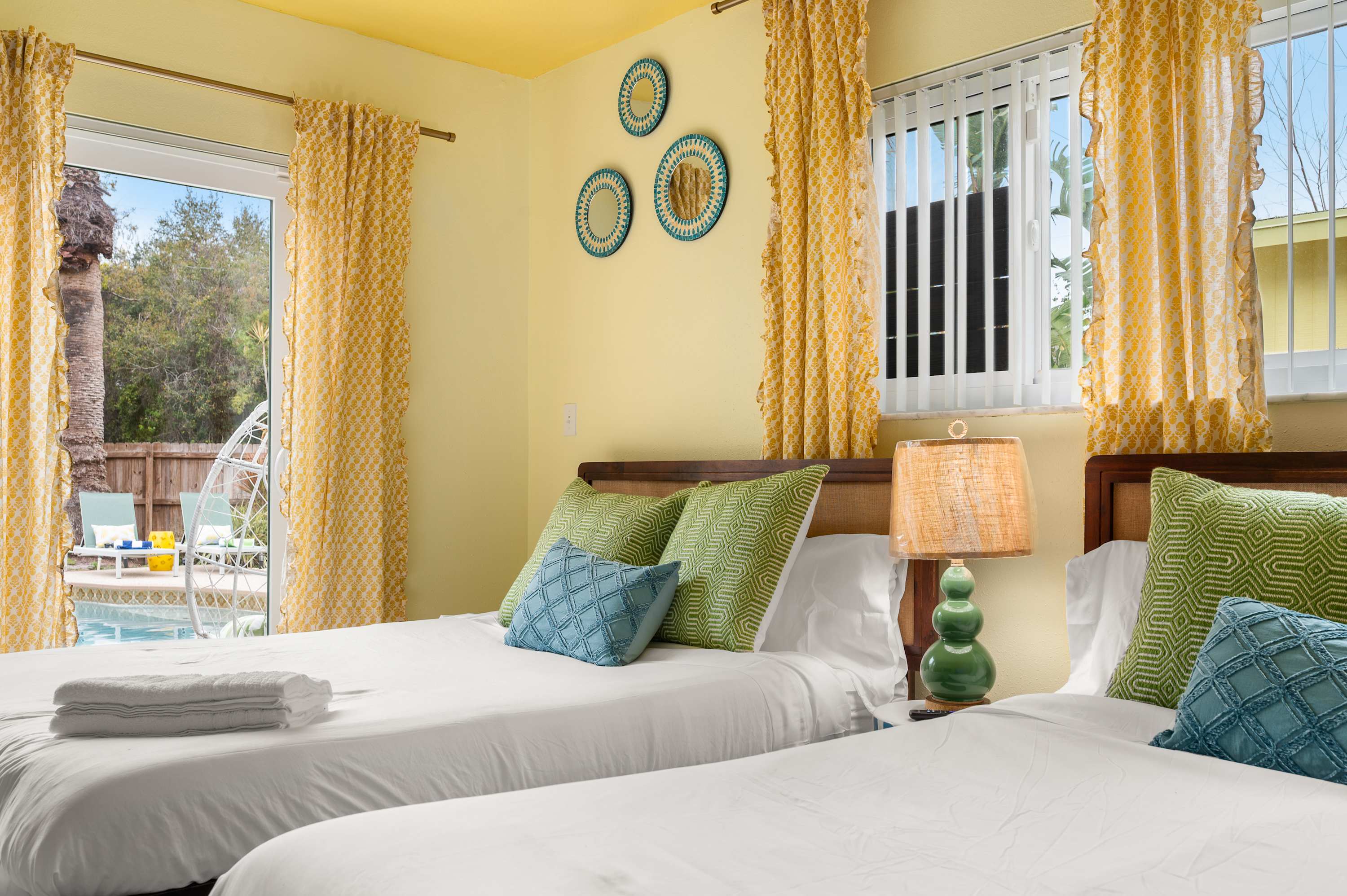 Bright bedroom w/ two beds, tropical plants & large windows.