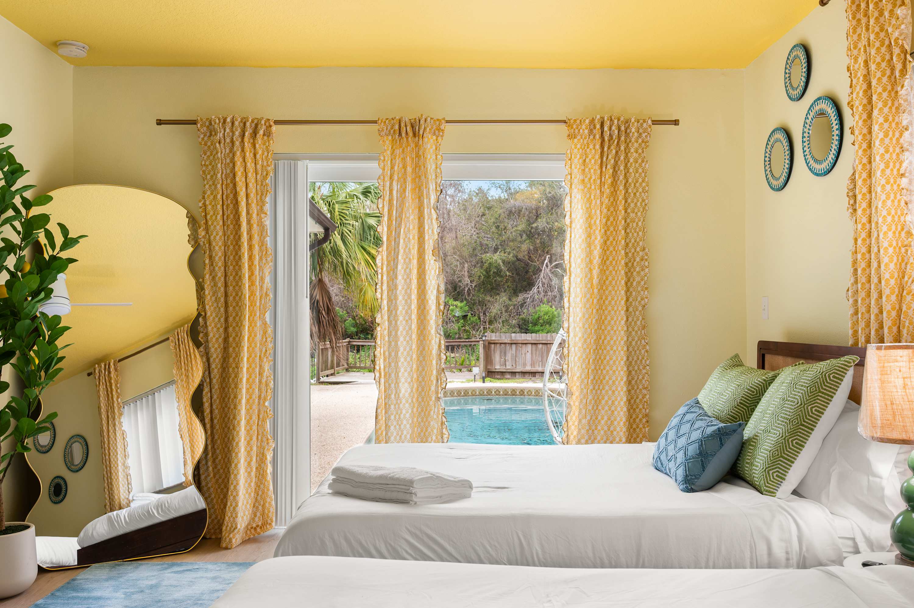 Sun-soaked bedroom w/ pool views, a bed & warm yellow walls.
