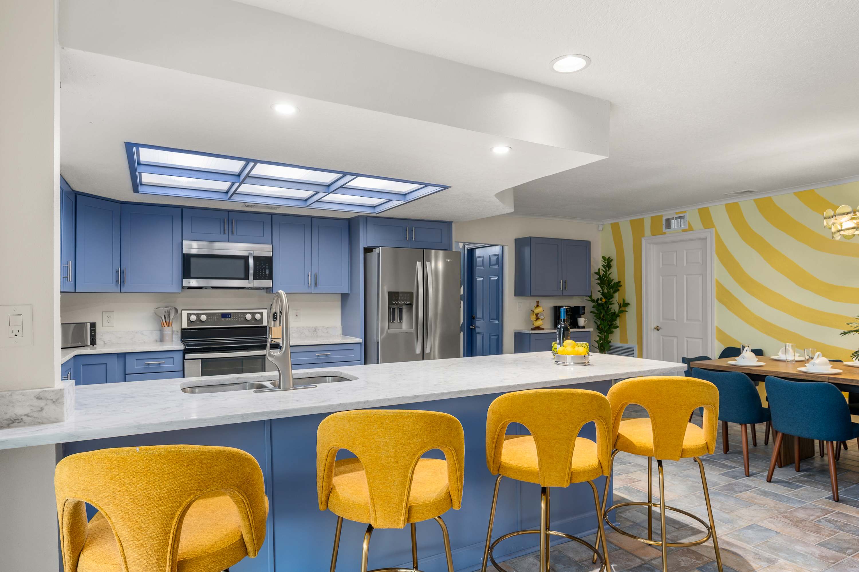 Bright kitchen w/ blue cabinets, yellow bar stools & skylight overhead.