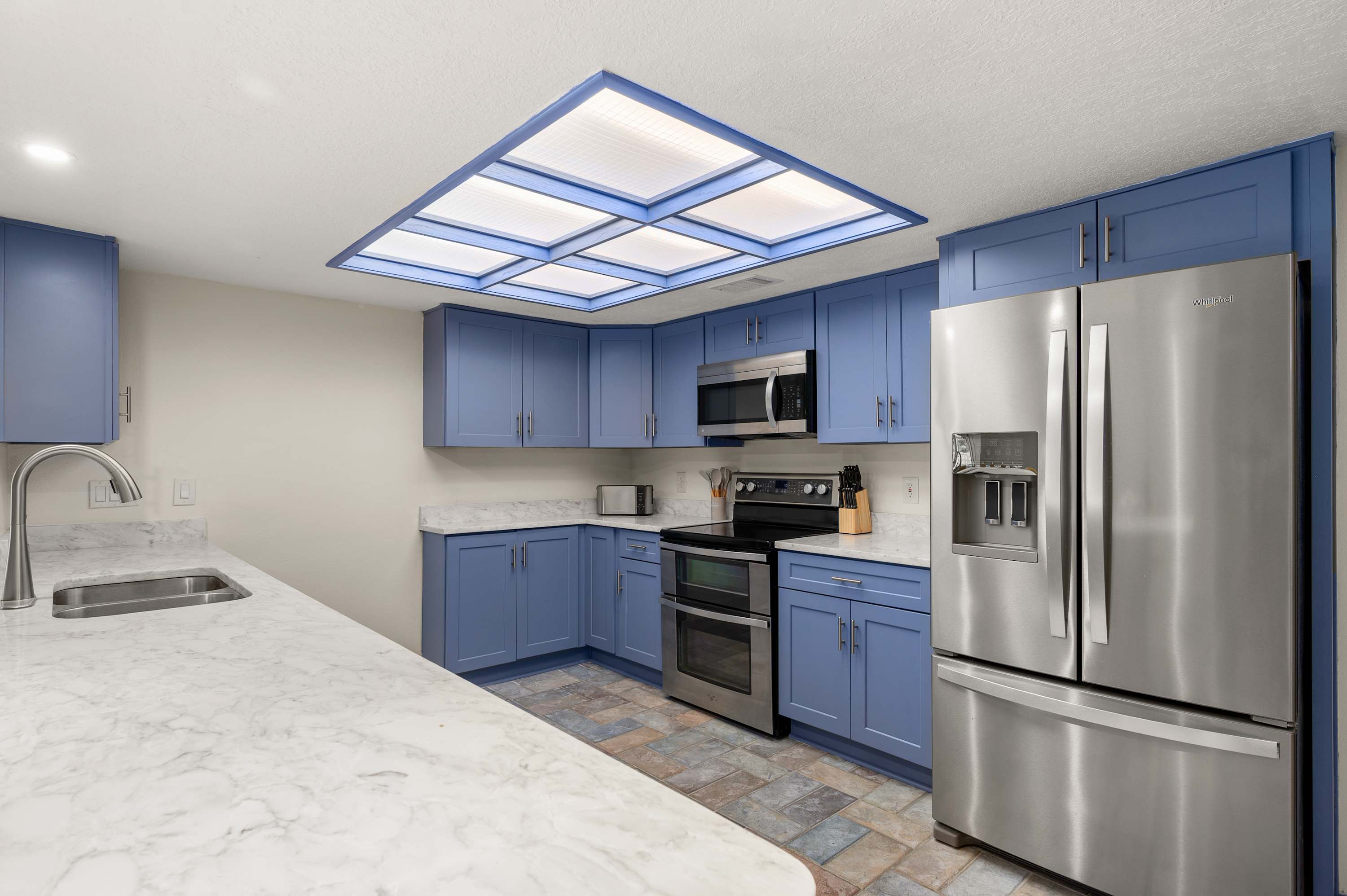 Spacious kitchen w/ stainless steel fridge, modern appliances & skylight.