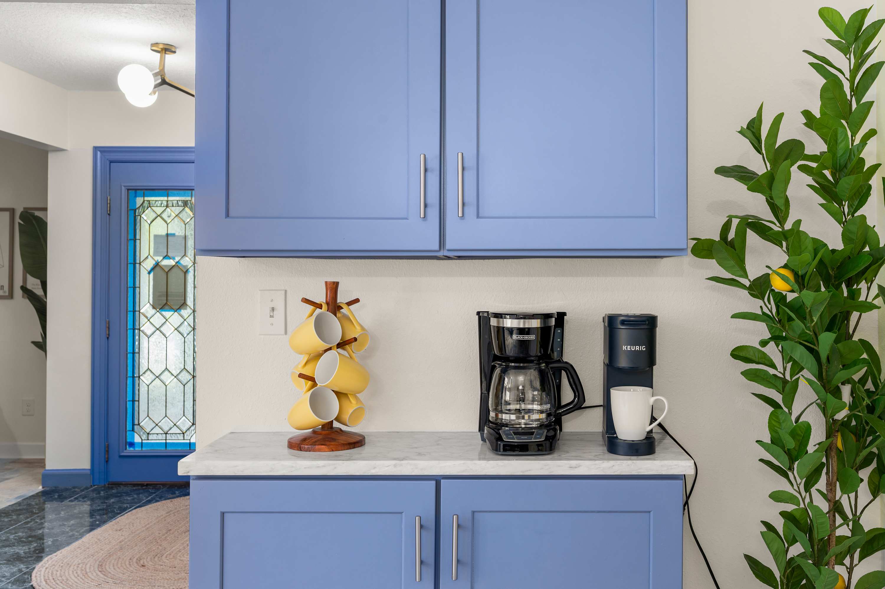 Kitchen nook w/ blue cabinetry, marble counters & a lush indoor plant.