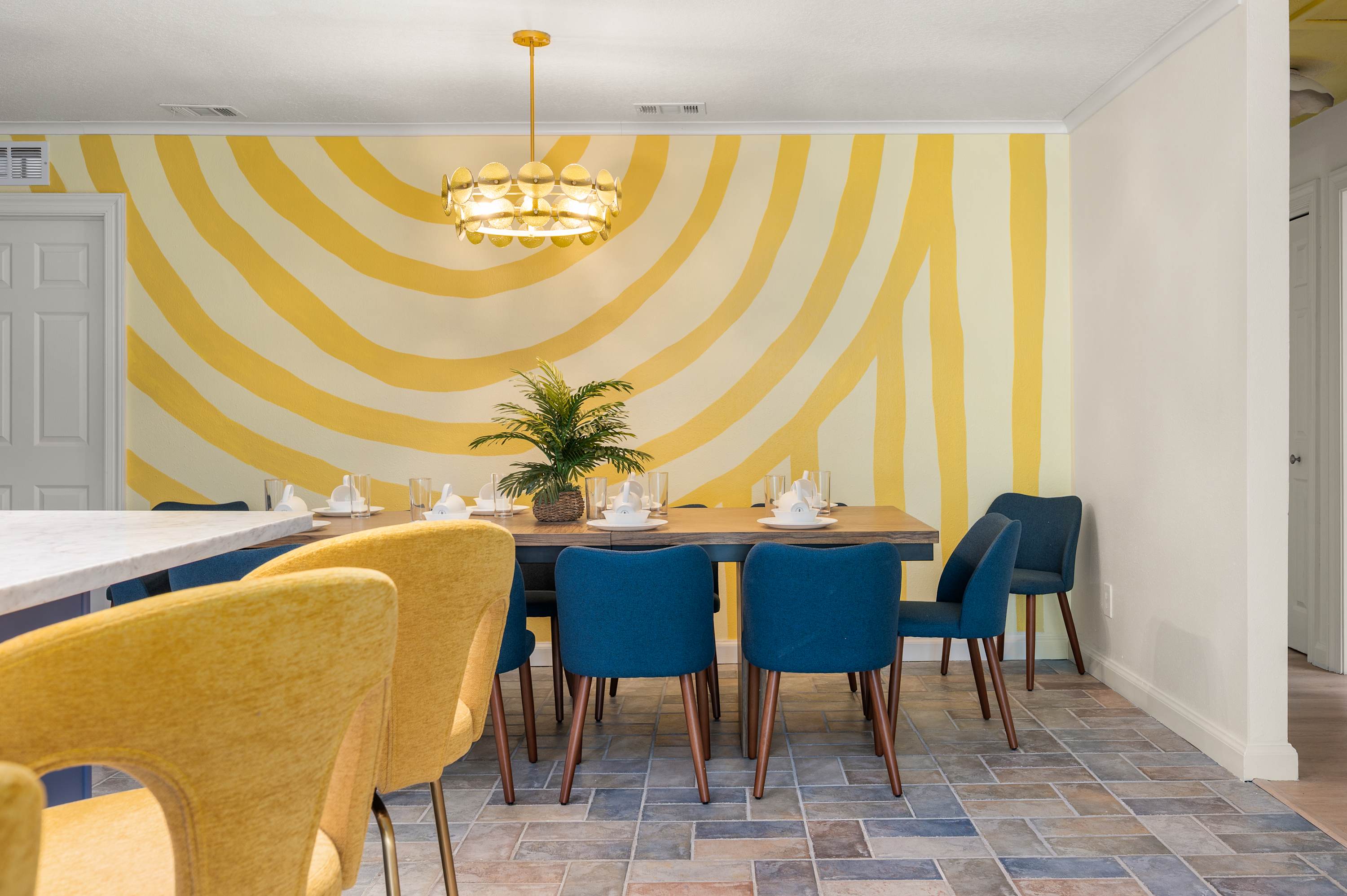 Elegant dining area w/ yellow sunburst wall, teal chairs & warm pendant light.