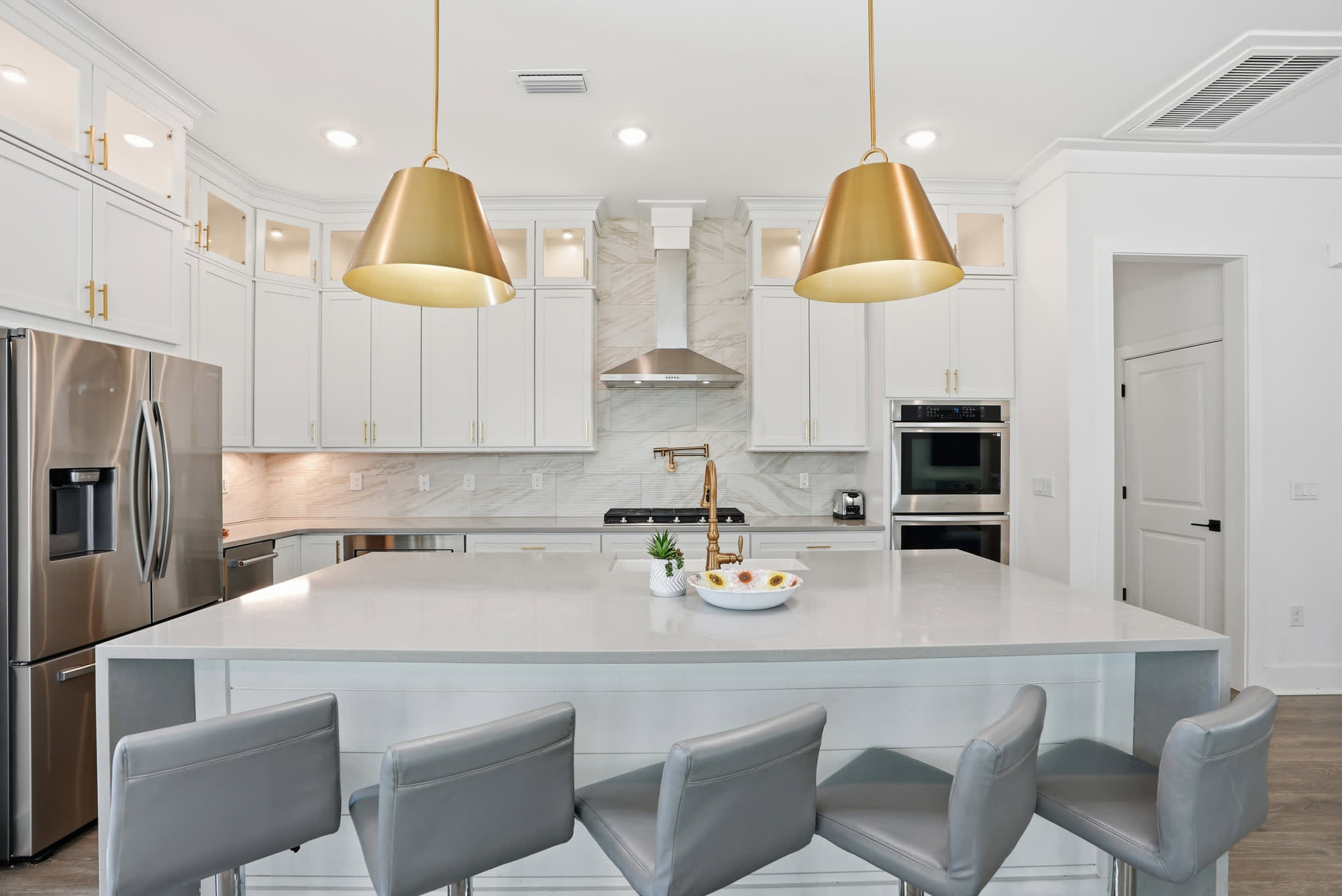120 Dune Drive – Modern kitchen with white cabinets, stainless steel appliances, large island, and two gold pendant lights.