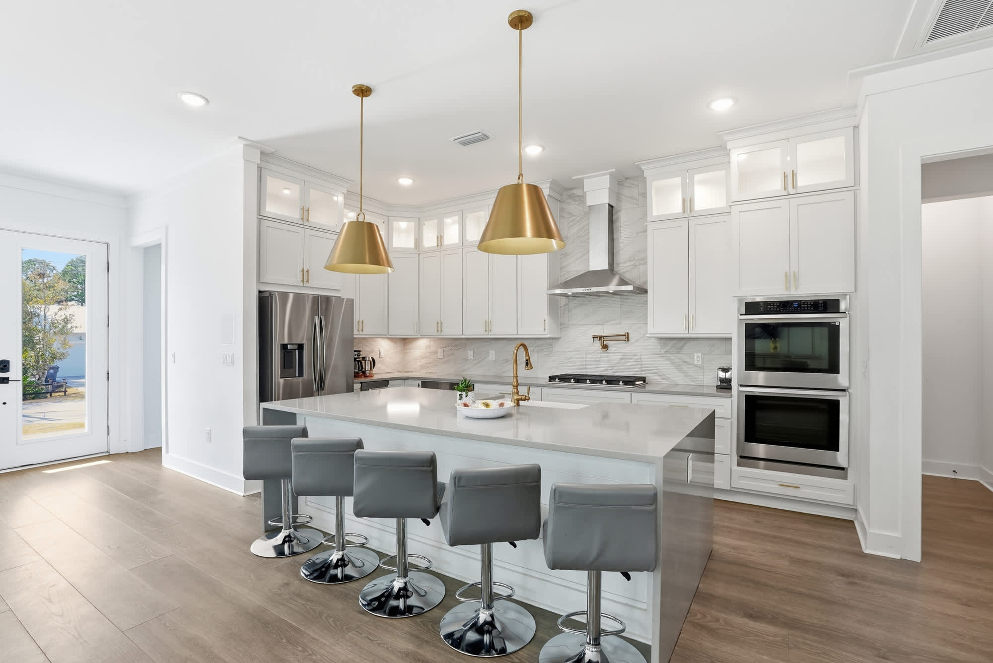 120 Dune Drive – Modern kitchen with gray stools, white cabinets, gold pendant lights, and stainless steel appliances.