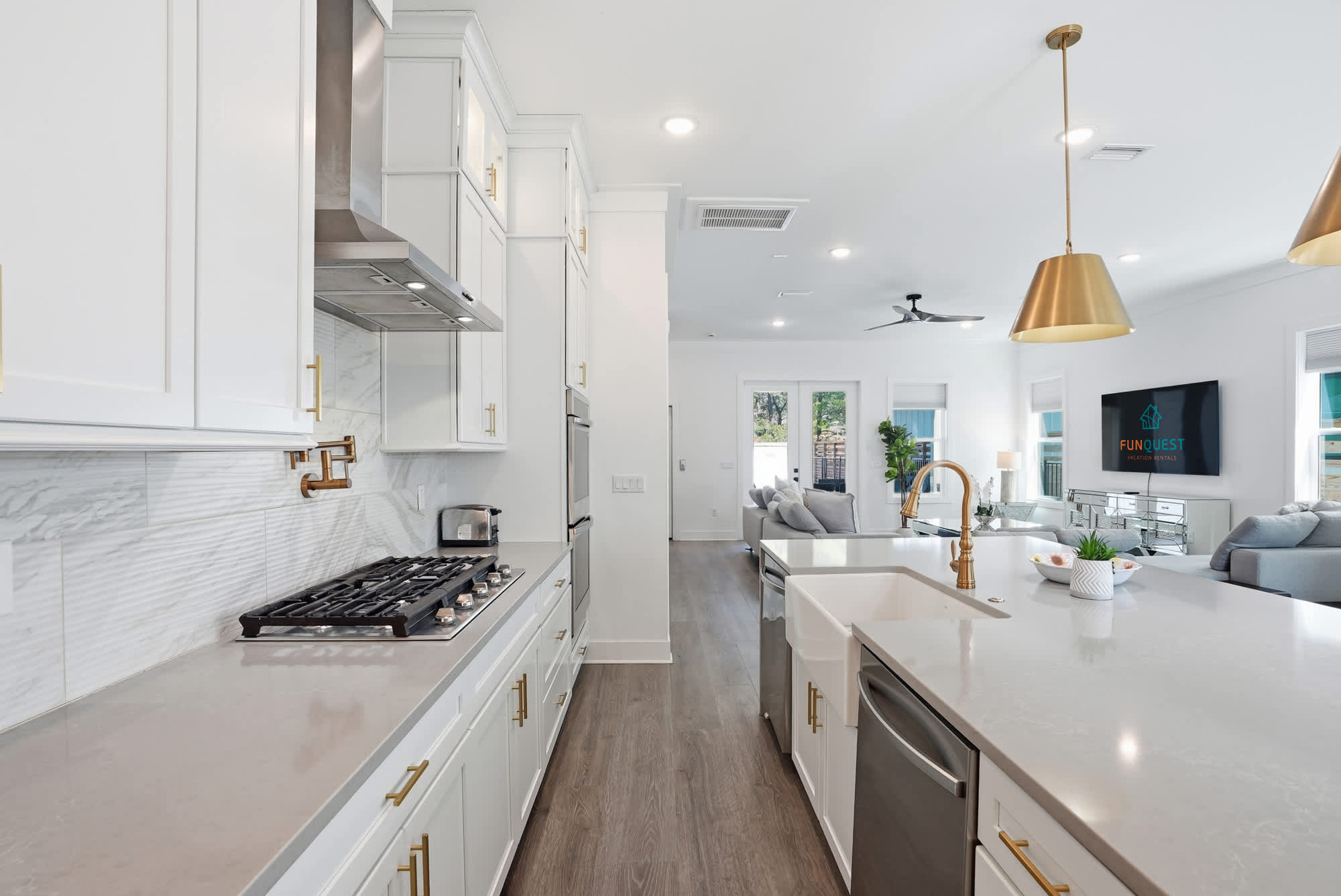 120 Dune Drive – Modern kitchen with white cabinets, gold accents, and open view to living area with light-colored furniture.