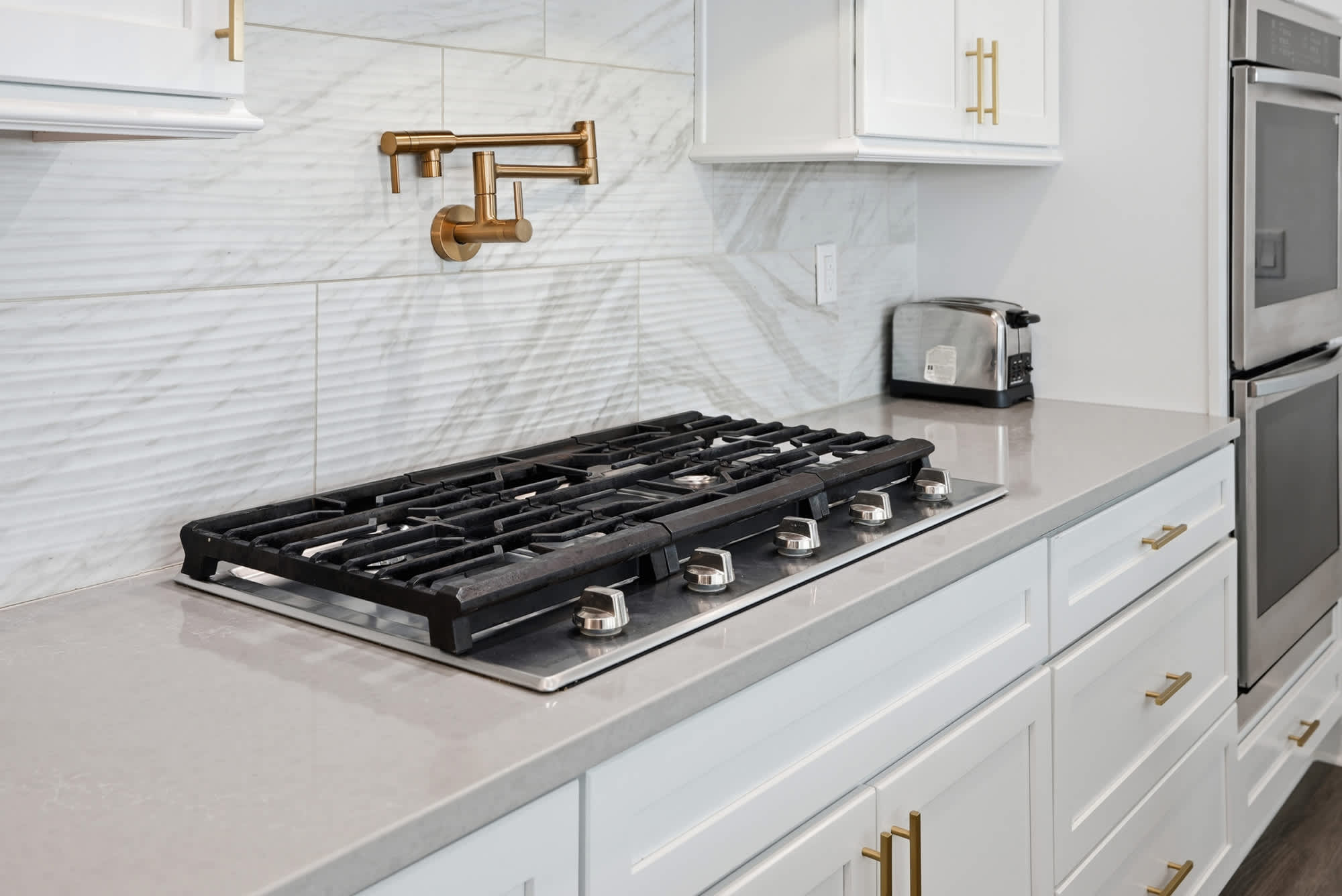 120 Dune Drive – Modern kitchen with a gas stove, white cabinets, gold fixtures, and stainless steel appliances.