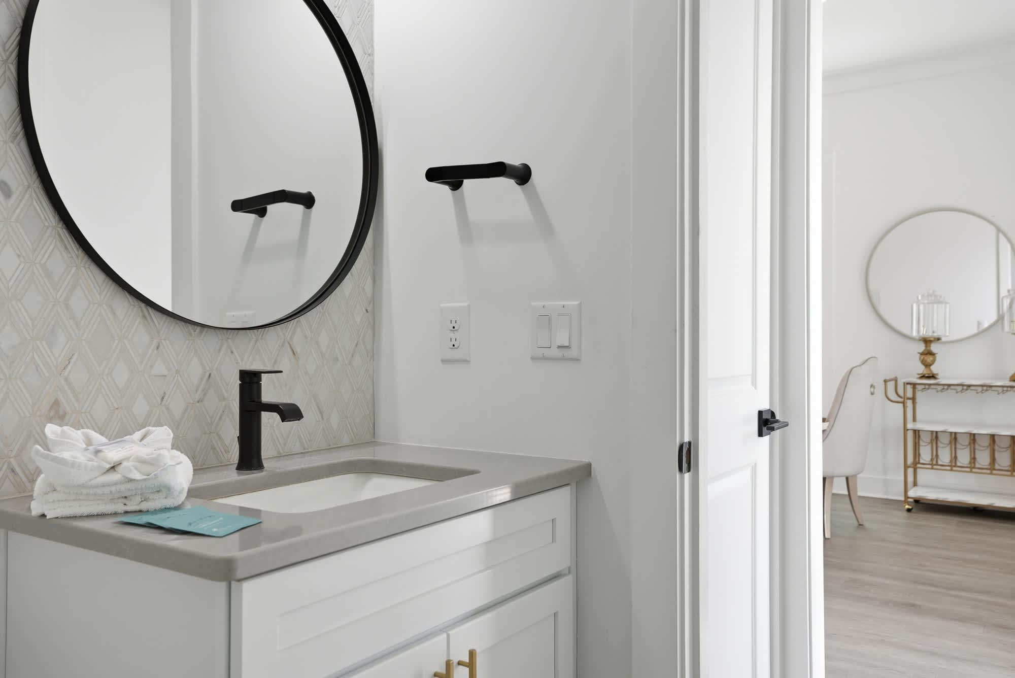 120 Dune Drive – Bright bathroom featuring a circular mirror, gray countertop, black faucet, and white cabinetry.