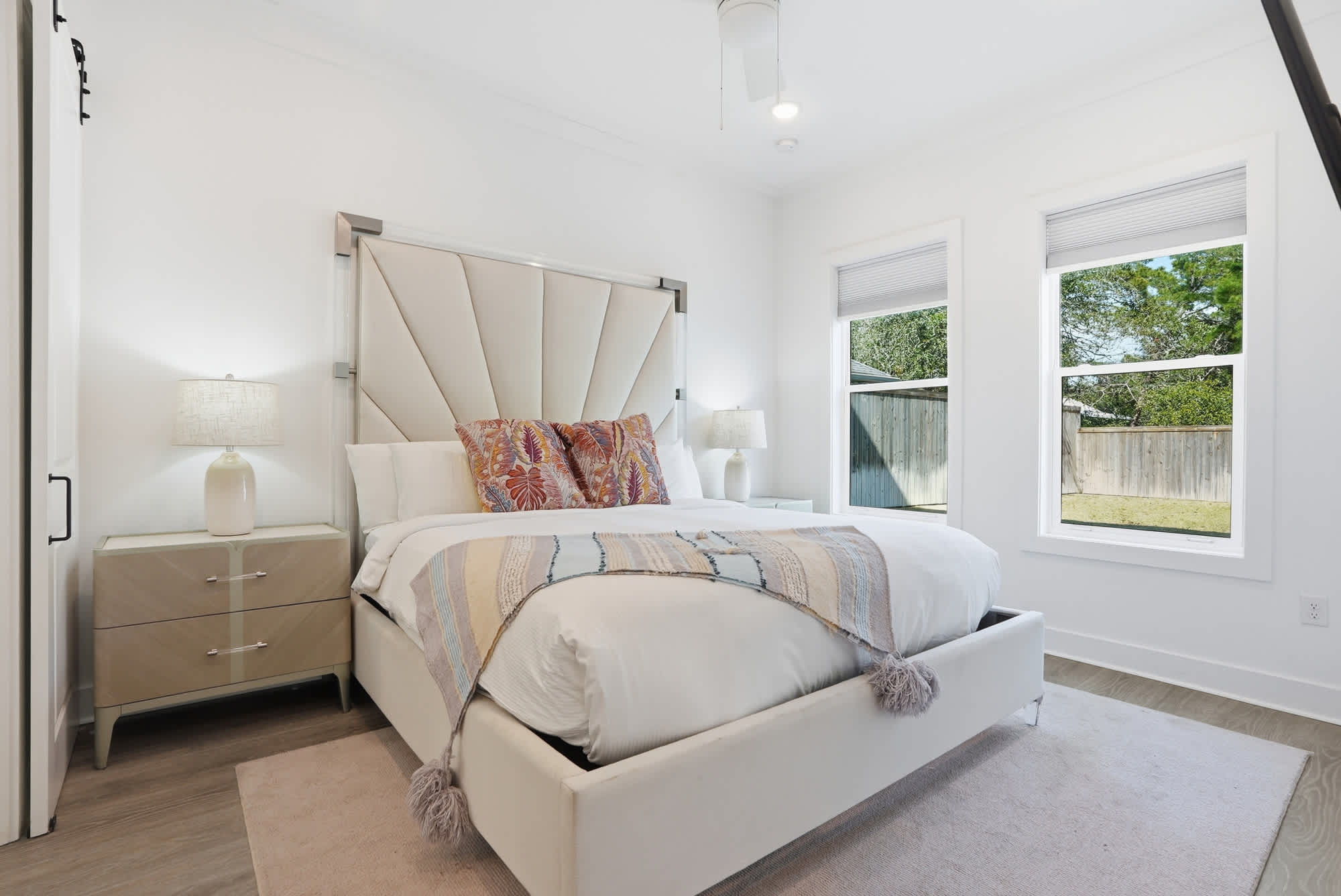 120 Dune Drive – Bright bedroom with a queen bed, bedside lamp, and windows overlooking a fenced yard.