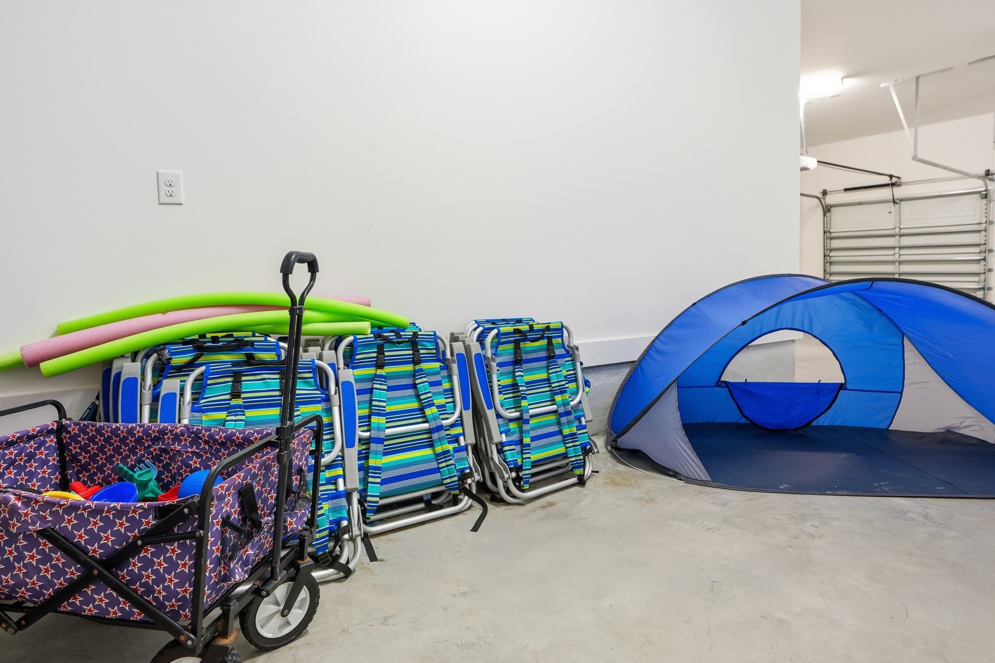 120 Dune Drive – Garage space with beach chairs, pool noodles, a cart, and a blue tent.