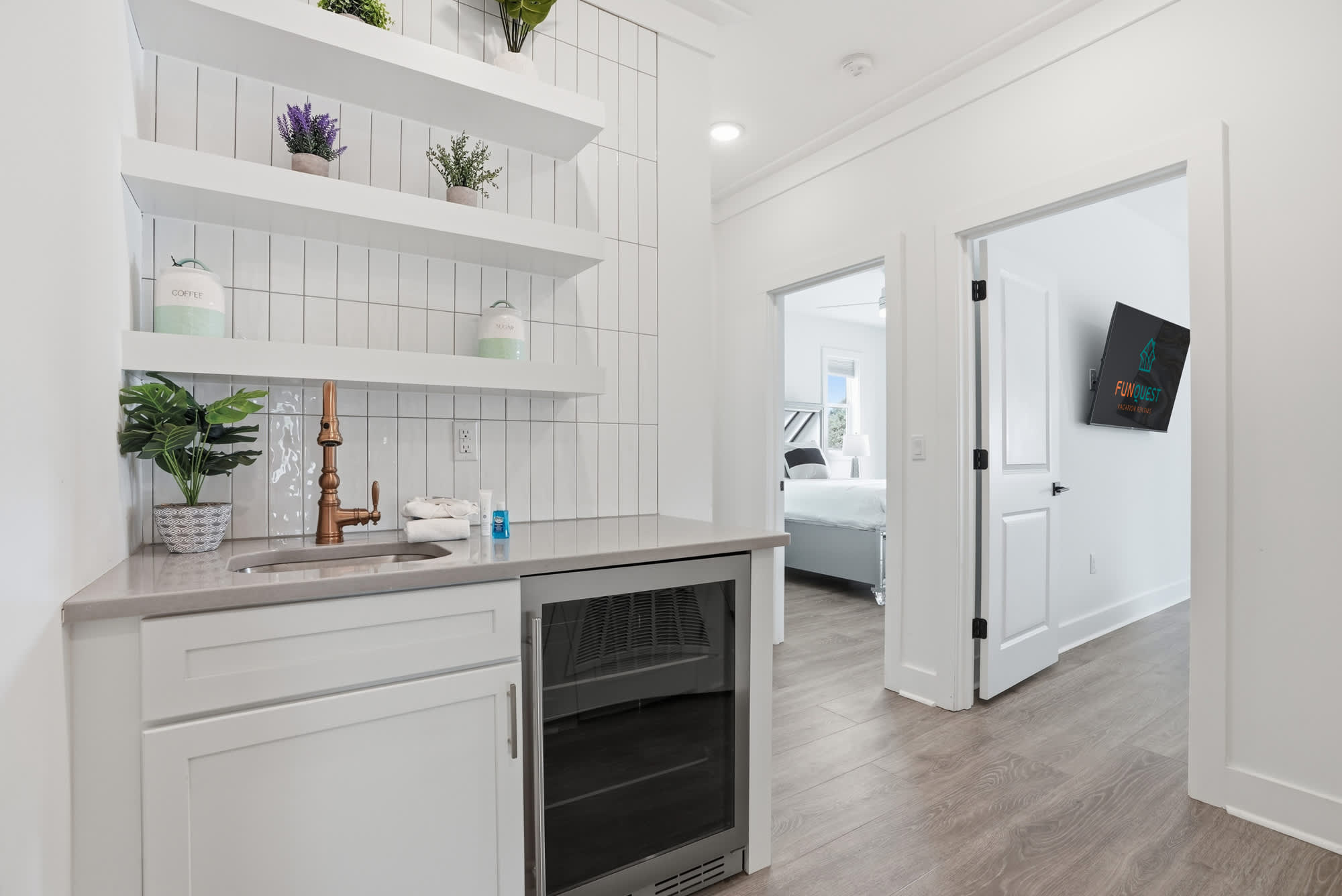 120 Dune Drive – Small kitchenette with shelves, sink, and refrigerator; doorway leading to a bedroom with a TV visible.