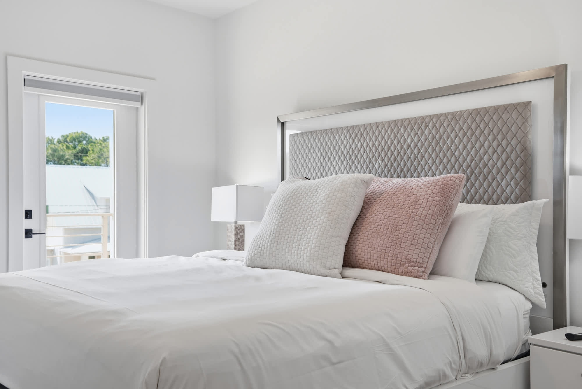 120 Dune Drive – Bright bedroom with a king-size bed, pink and white pillows, nightstand, and door to a balcony.