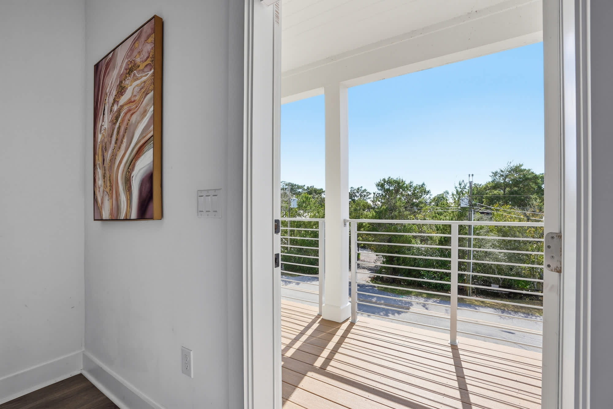 120 Dune Drive – View from an open doorway onto a balcony with railing and greenery outside.