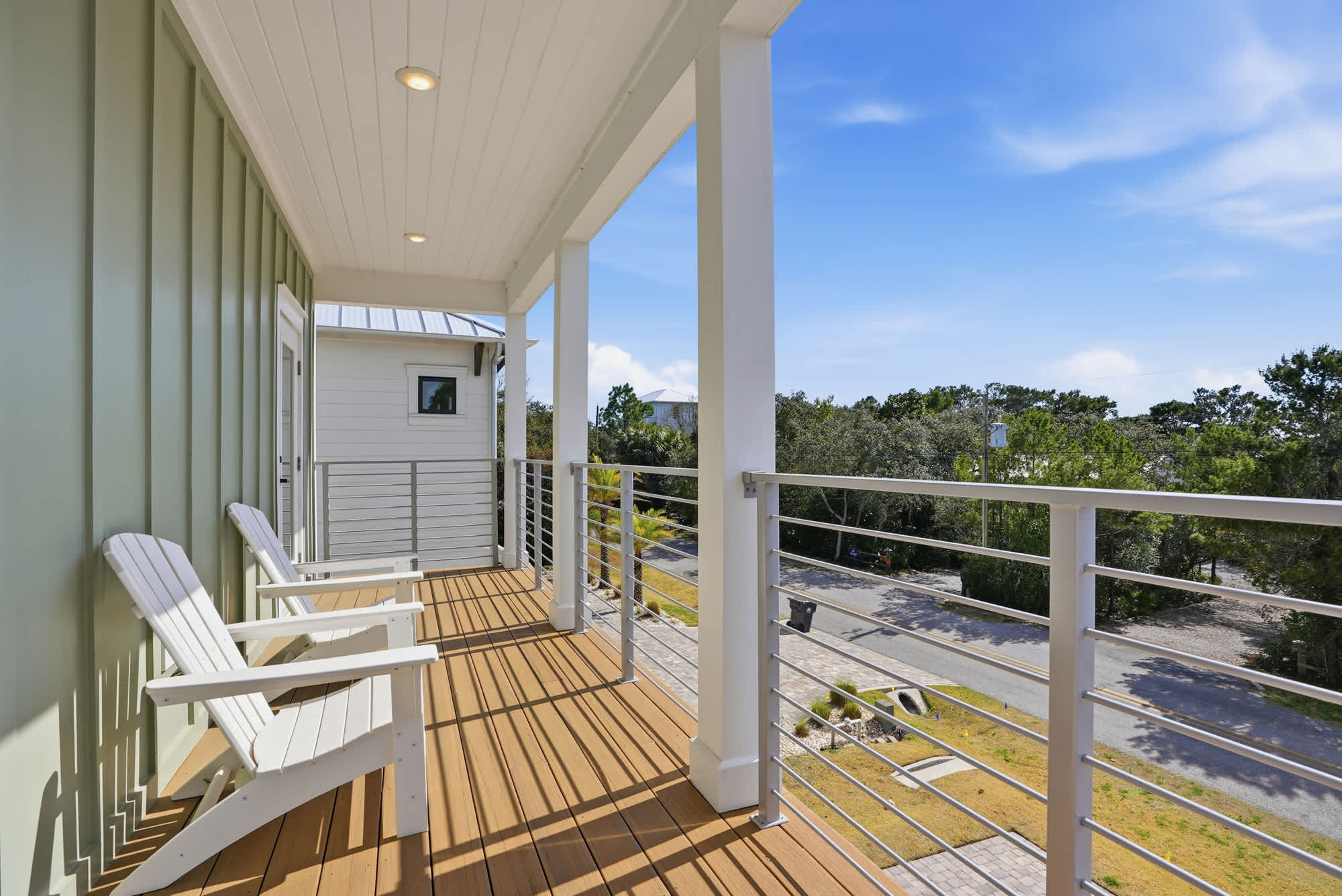 120 Dune Drive – Covered balcony with two white chairs and a view of surrounding greenery and a road.