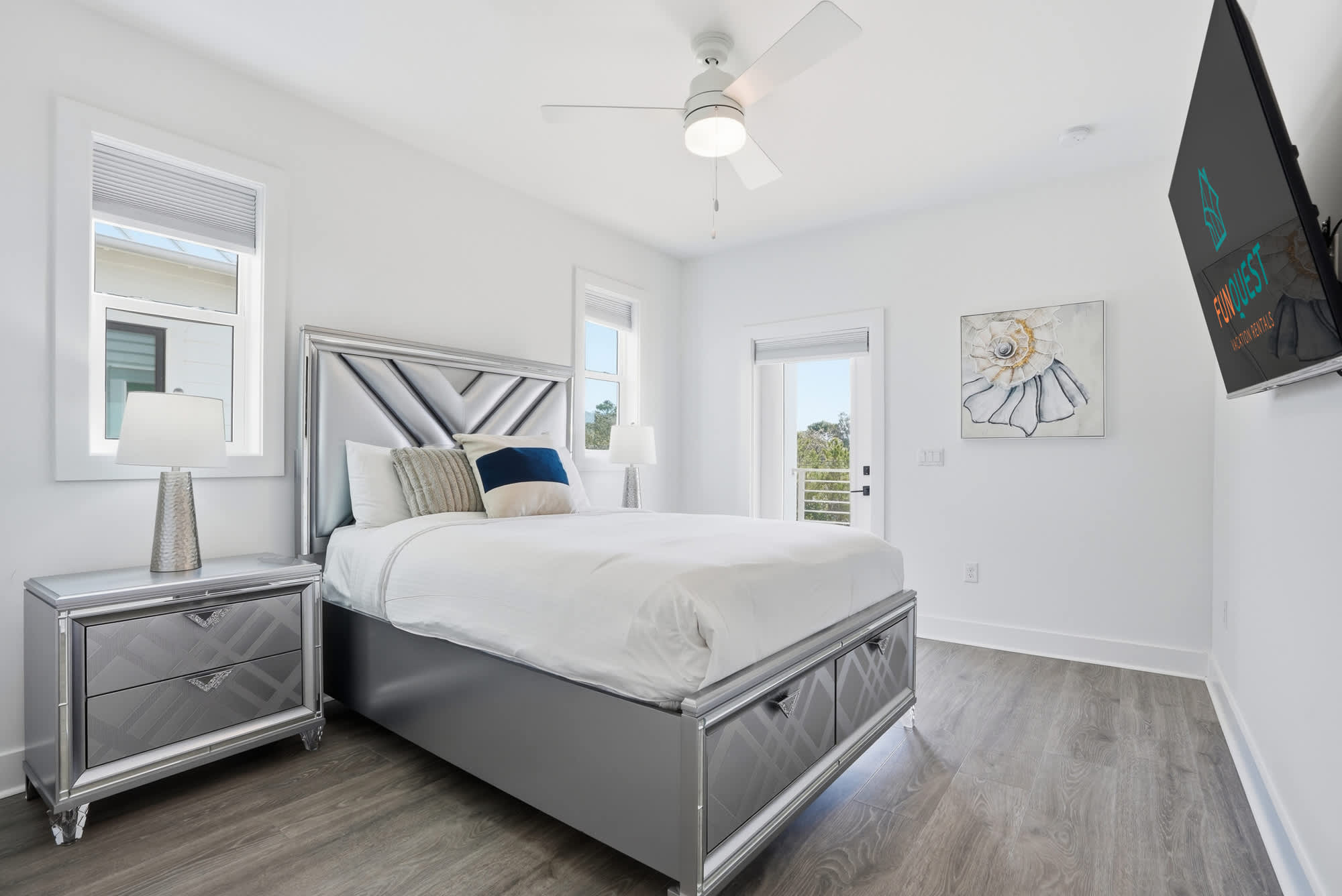 120 Dune Drive – Bright bedroom with a silver bed frame, nightstand, ceiling fan, and large windows.
