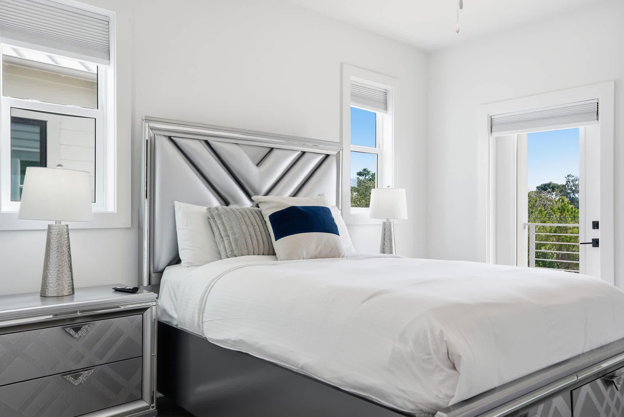 120 Dune Drive – Bright bedroom with a silver bed frame, bedside lamps, and windows showing greenery outside.