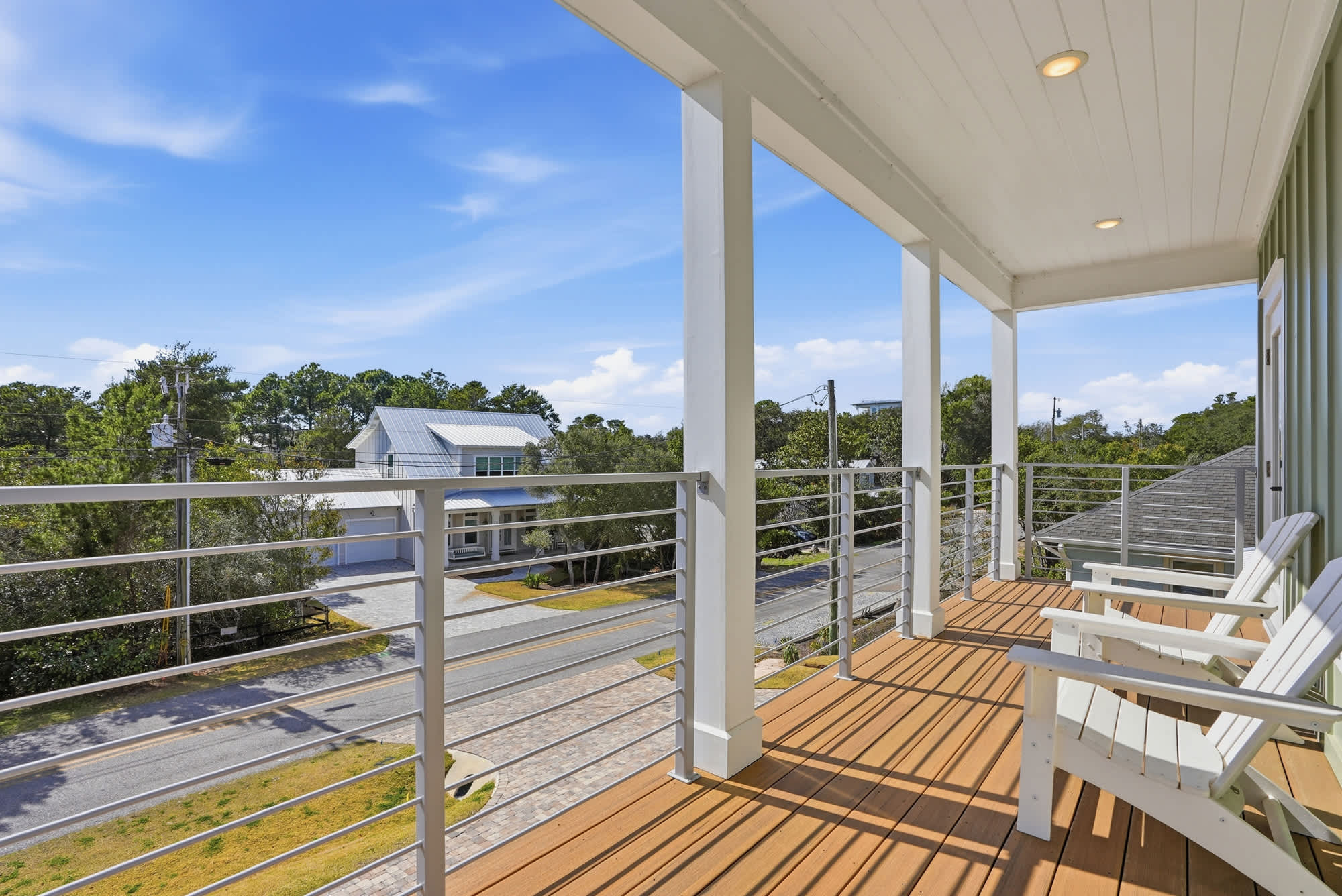 120 Dune Drive – balcony with two white chairs, overlooking a street and nearby houses, under a blue sky