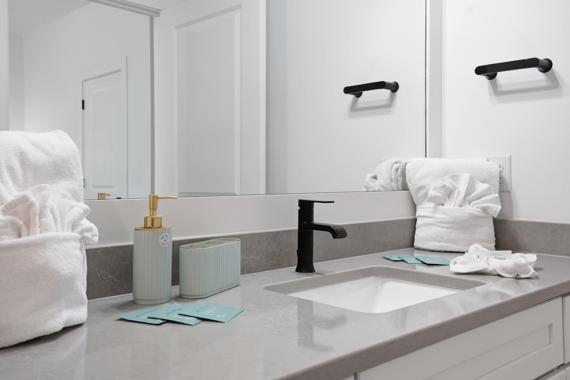 120 Dune Drive – Modern bathroom with gray countertop, black faucet, and neatly arranged towels and toiletries.