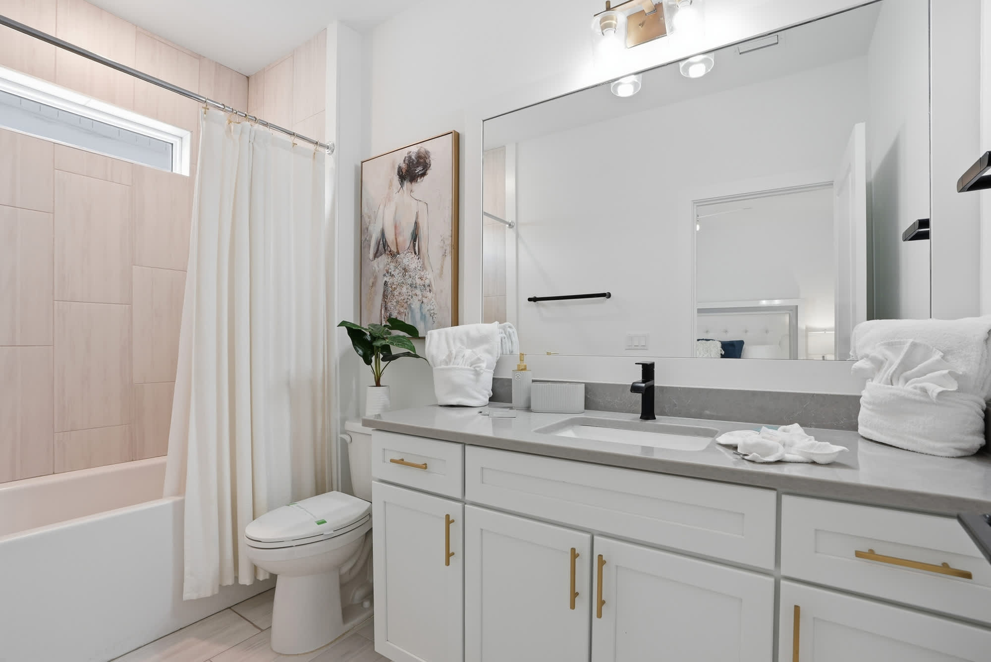 120 Dune Drive – Bright bathroom with a white tub, gray countertop, and a large mirror featuring a decorative painting.