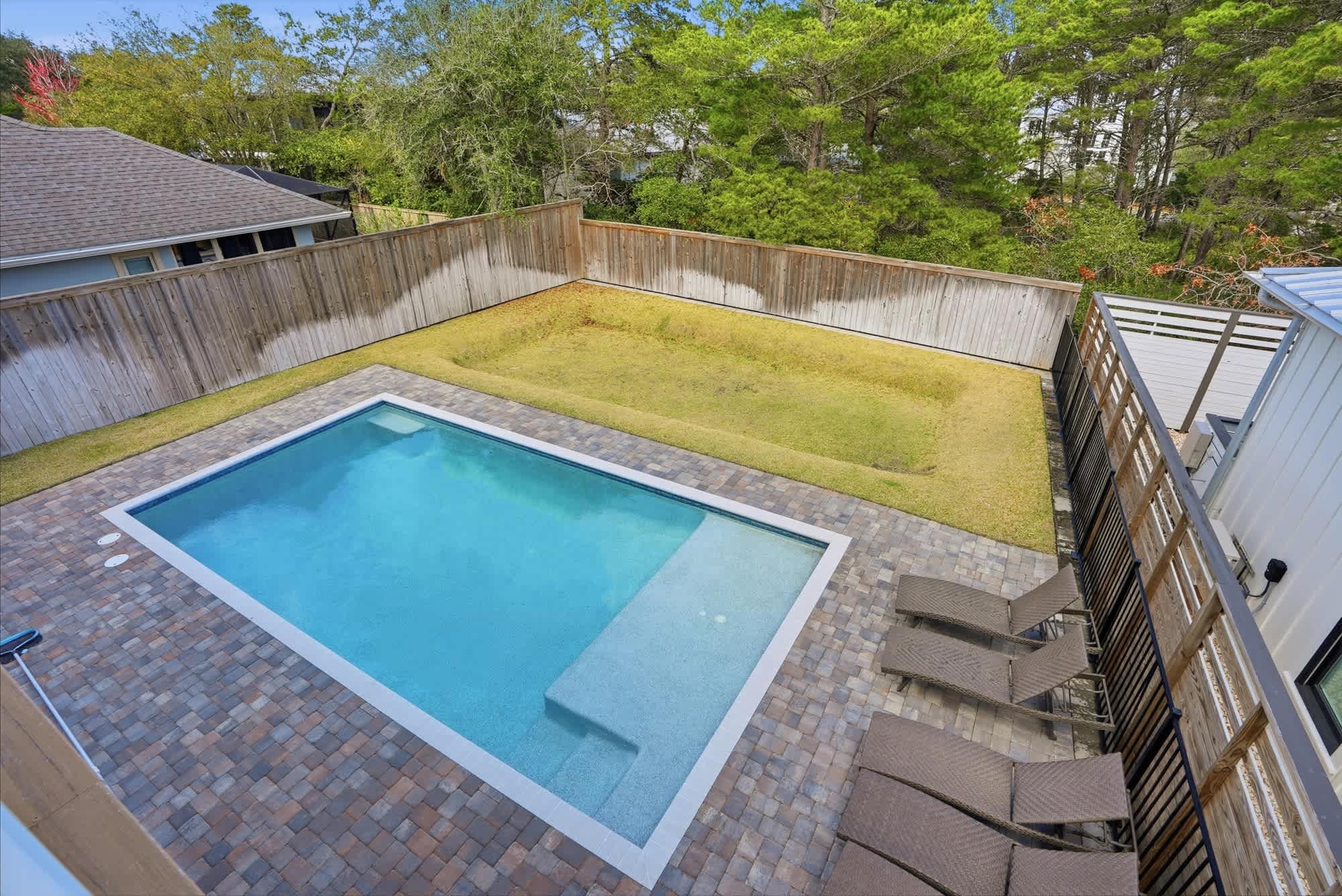 120 Dune Drive – Aerial view of a backyard with a swimming pool and lounge chairs surrounded by a wooden fence and greenery.