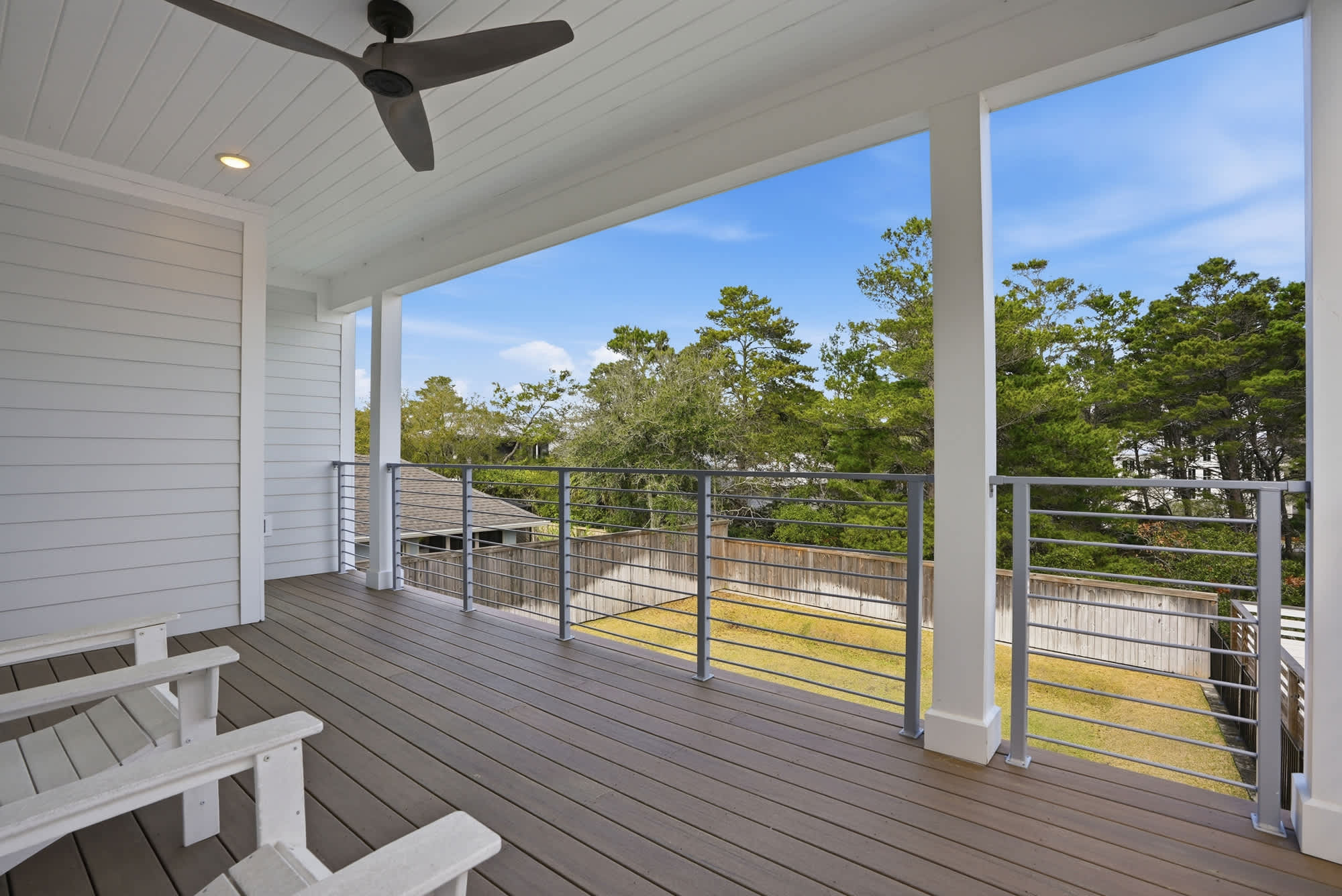 120 Dune Drive – Covered porch with wooden flooring, white railing, ceiling fan, and views of trees and lawn.