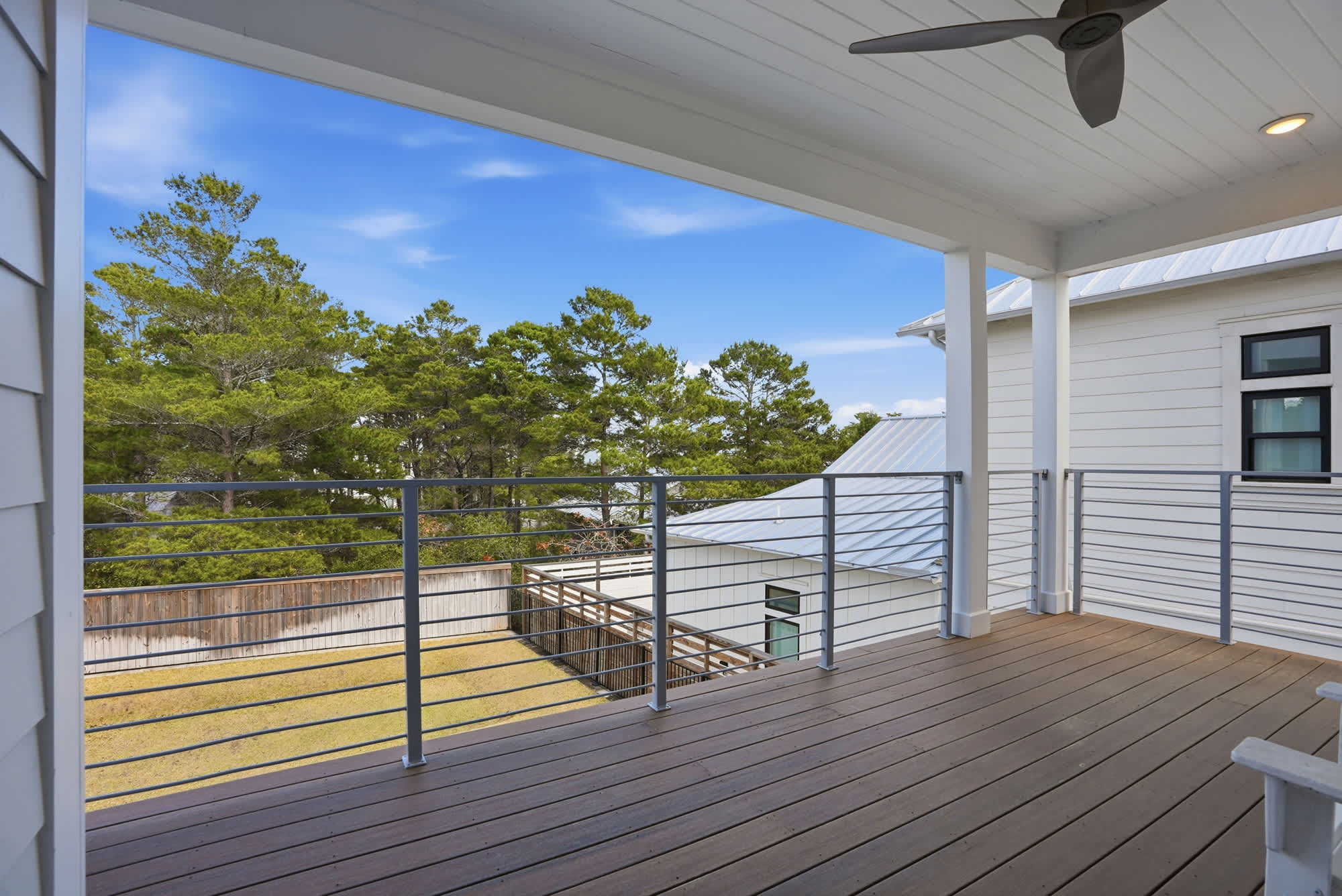 120 Dune Drive – Covered balcony with wooden floor, metal railing, and view of trees and neighboring structures.