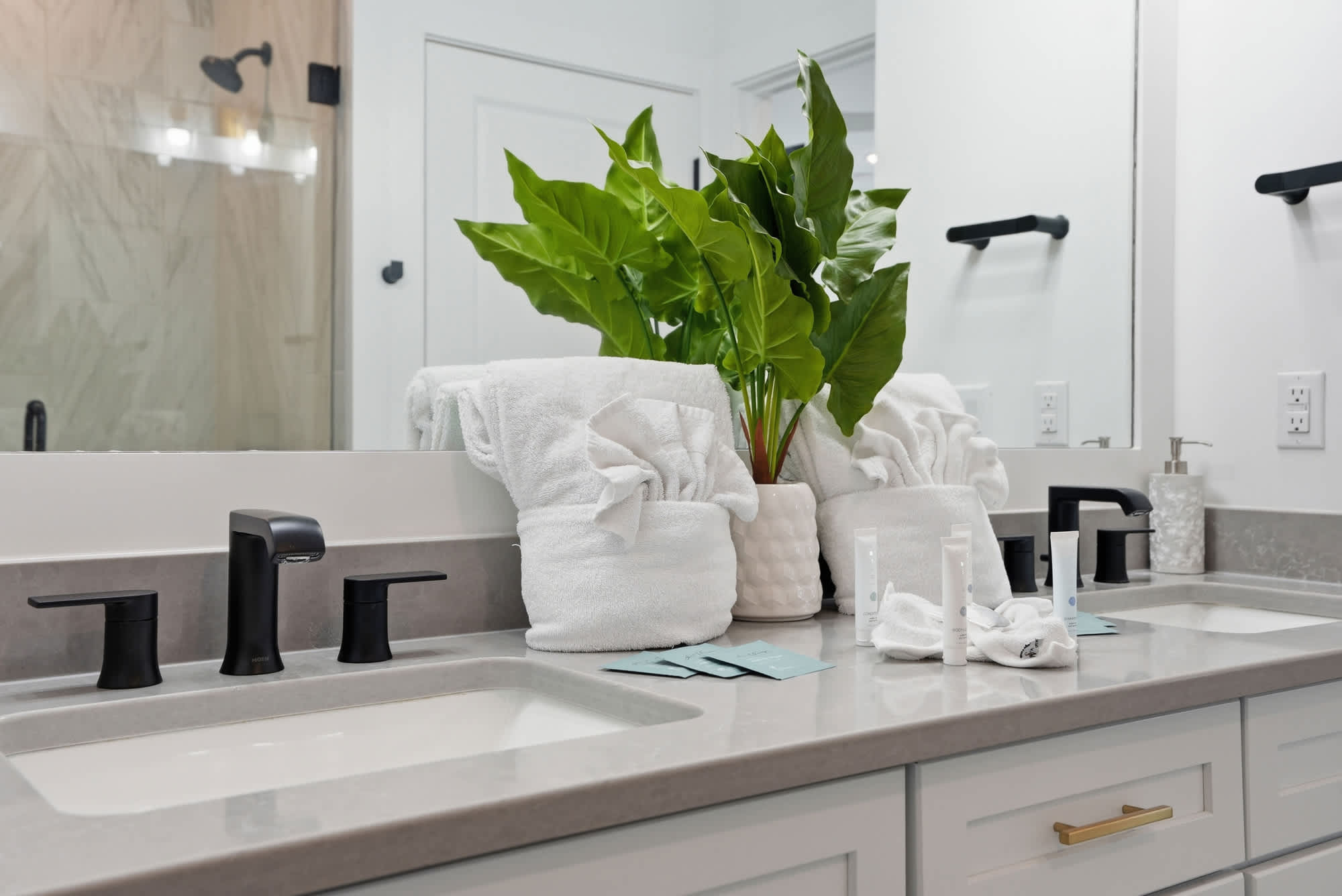 120 Dune Drive – Modern bathroom with a double sink, black fixtures, fresh towels, and a potted plant on the counter.