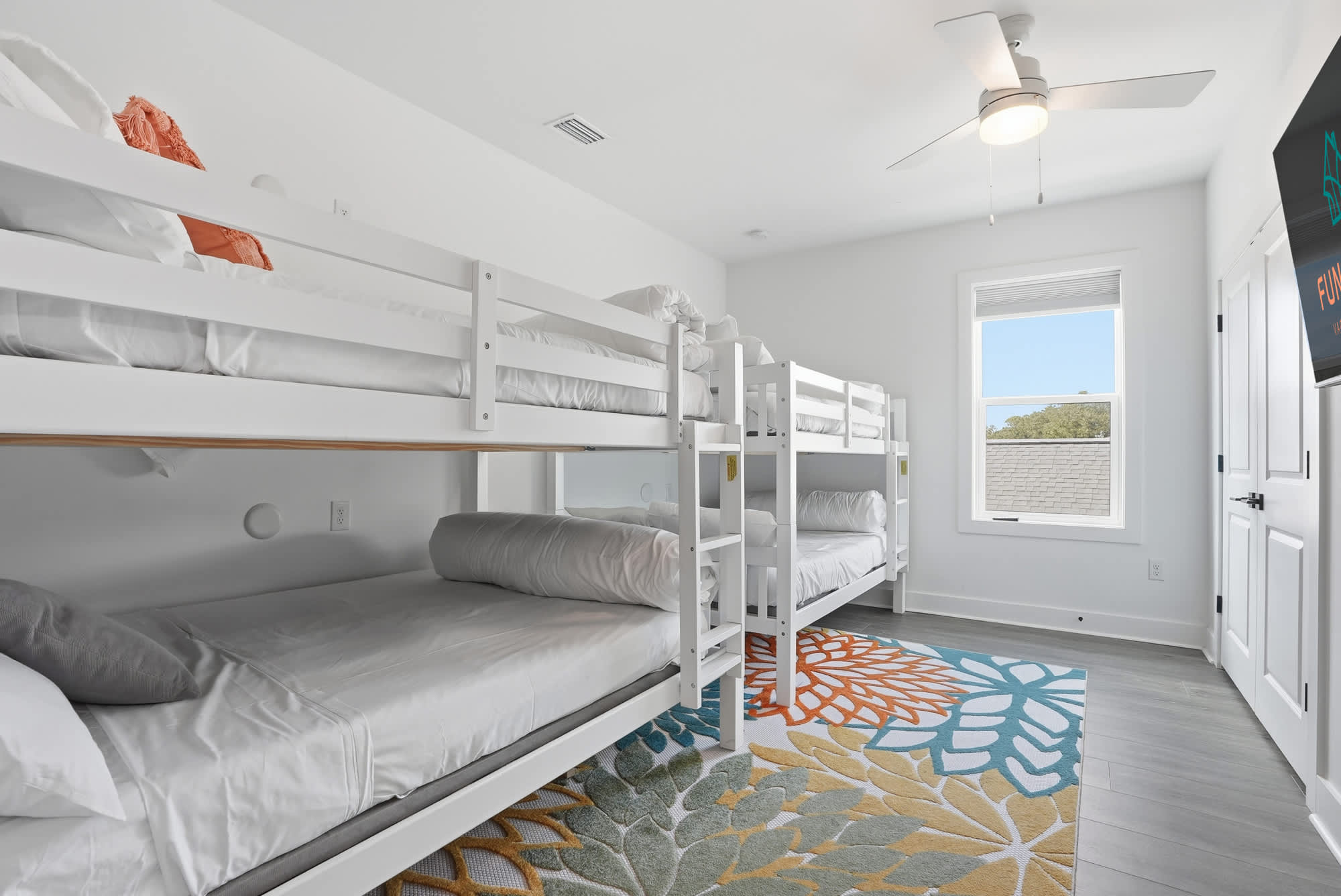 120 Dune Drive – Bunk room with two sets of white bunk beds, colorful area rug, and window.