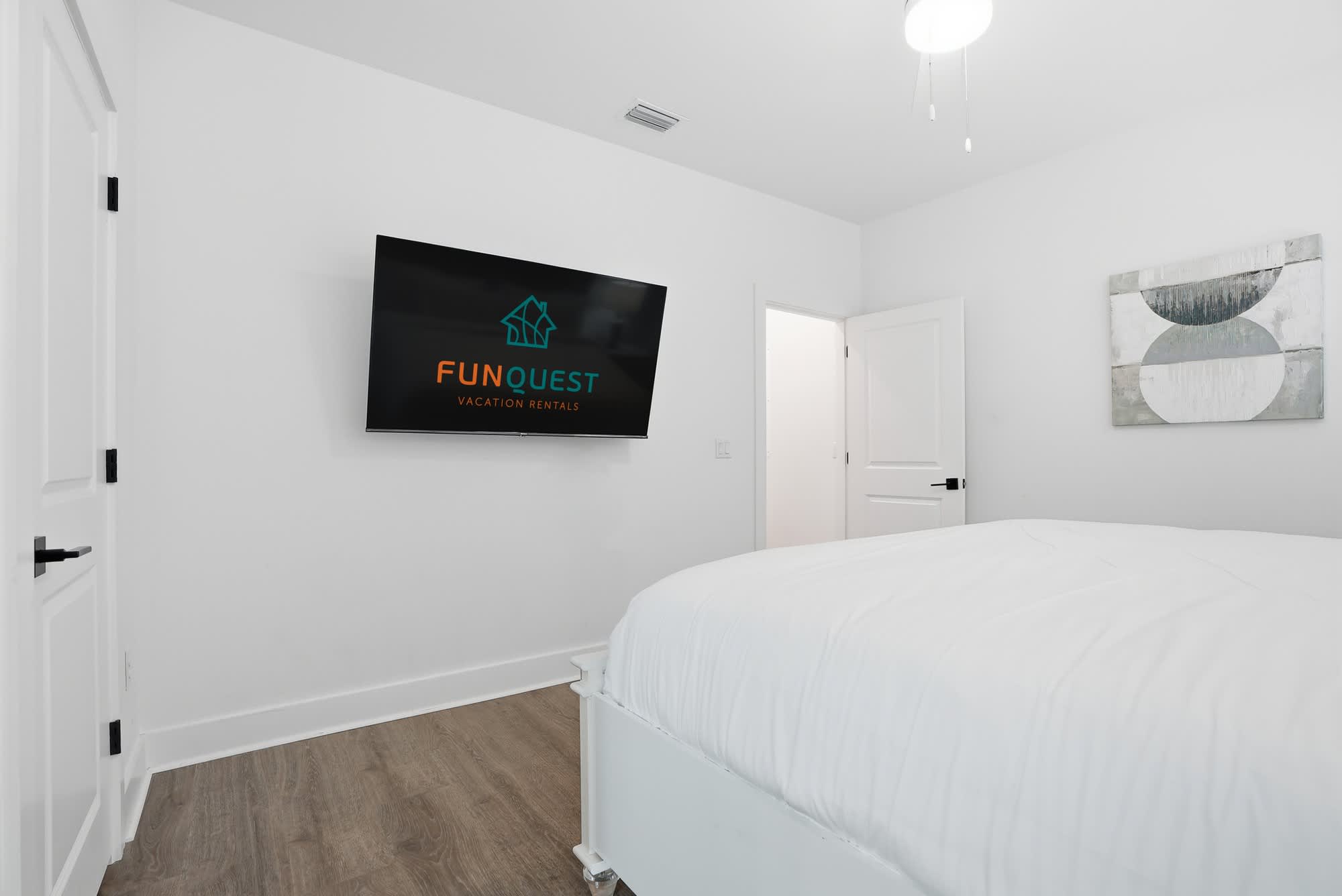 120 Dune Drive – Bedroom with a white bed, wall-mounted TV, and abstract wall art.
