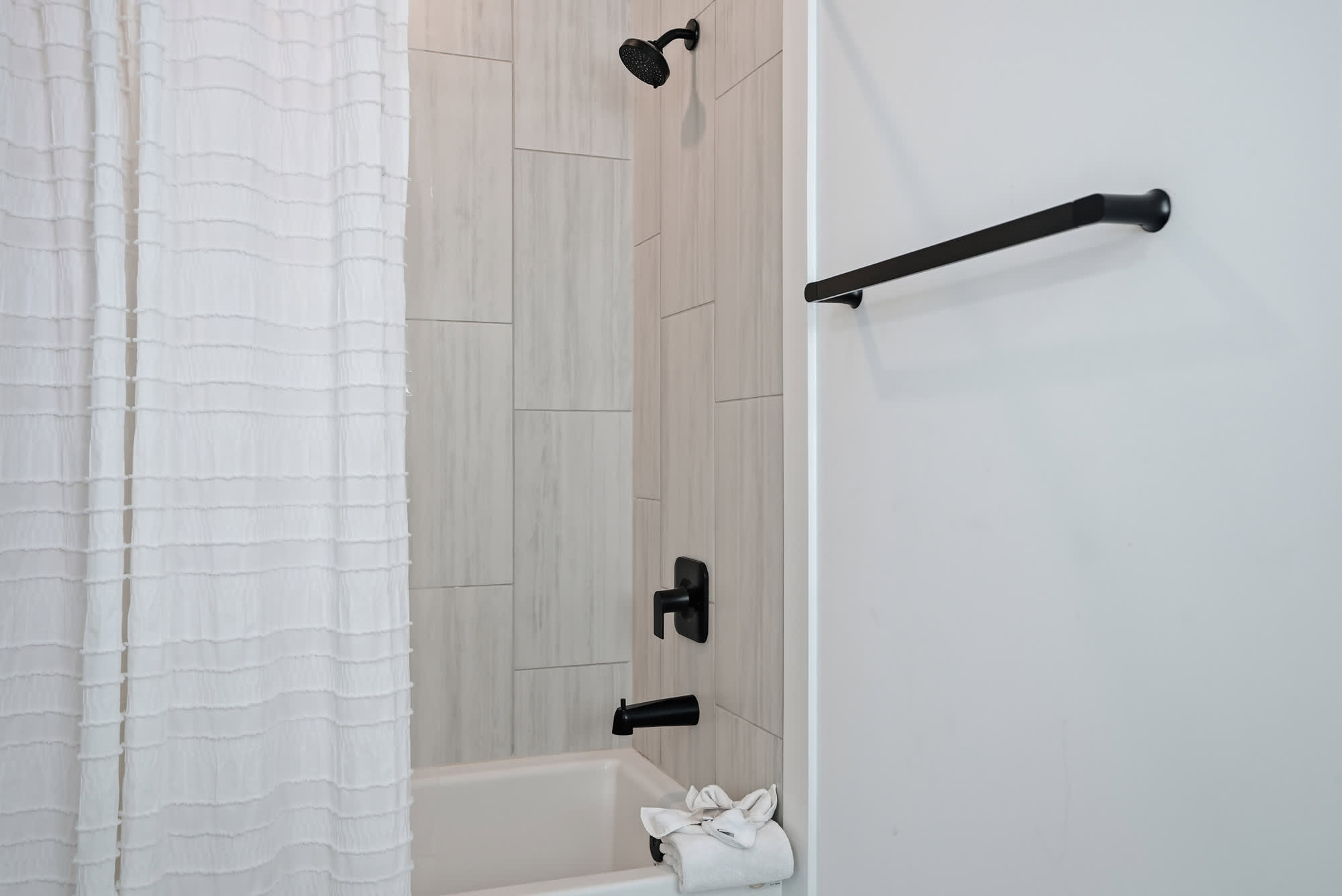 120 Dune Drive – Shower area with white curtain, black fixtures, and tiled walls.